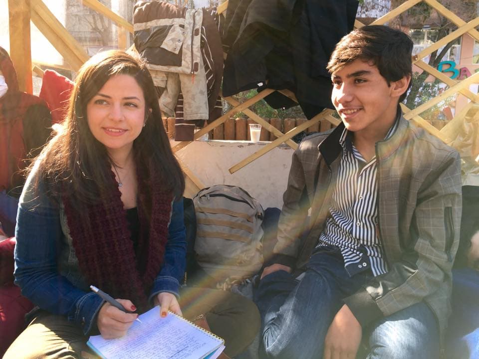 A reporter and teenage male sitting cross-legged on the ground for an interview