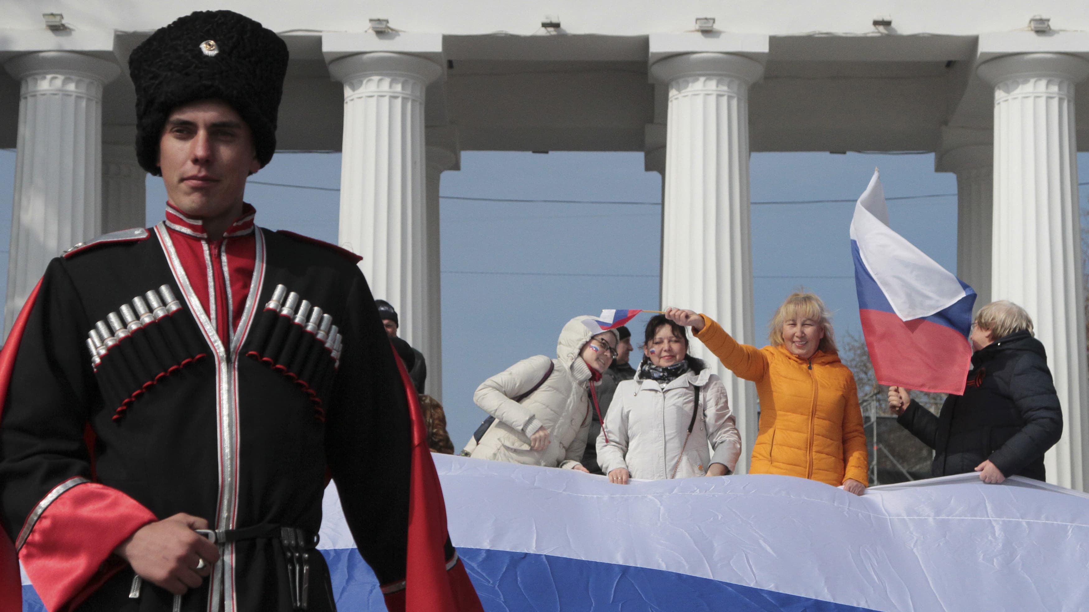 A Russian soldier stands in the foreground of citizens celebrating, waving flags