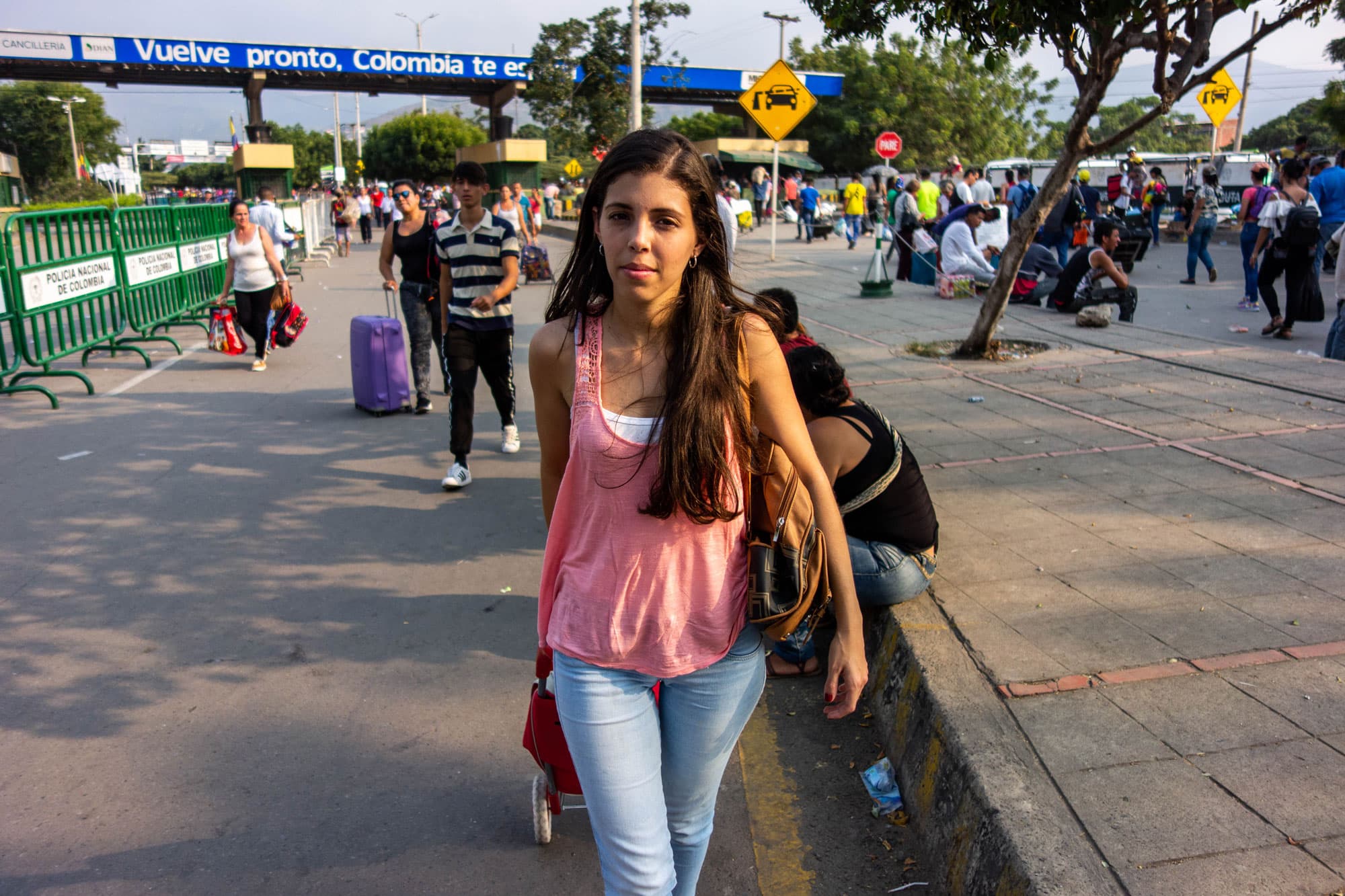 A woman wearing jeans and pink tank tops pulls luggage.