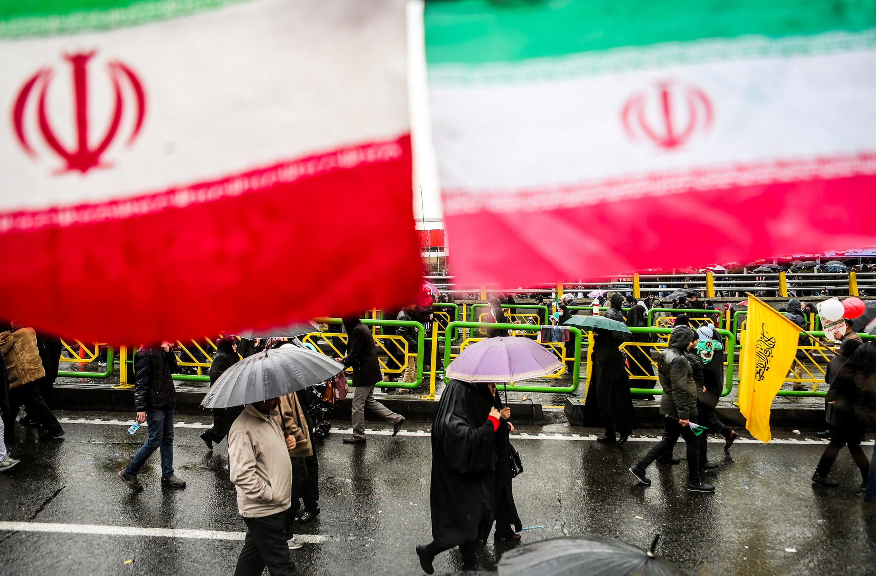 Iranian people carry umbrellas under giant Iranian flags