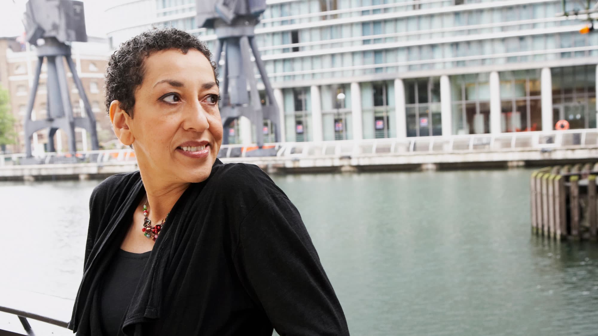 A woman looks back over a river with a building behind her.