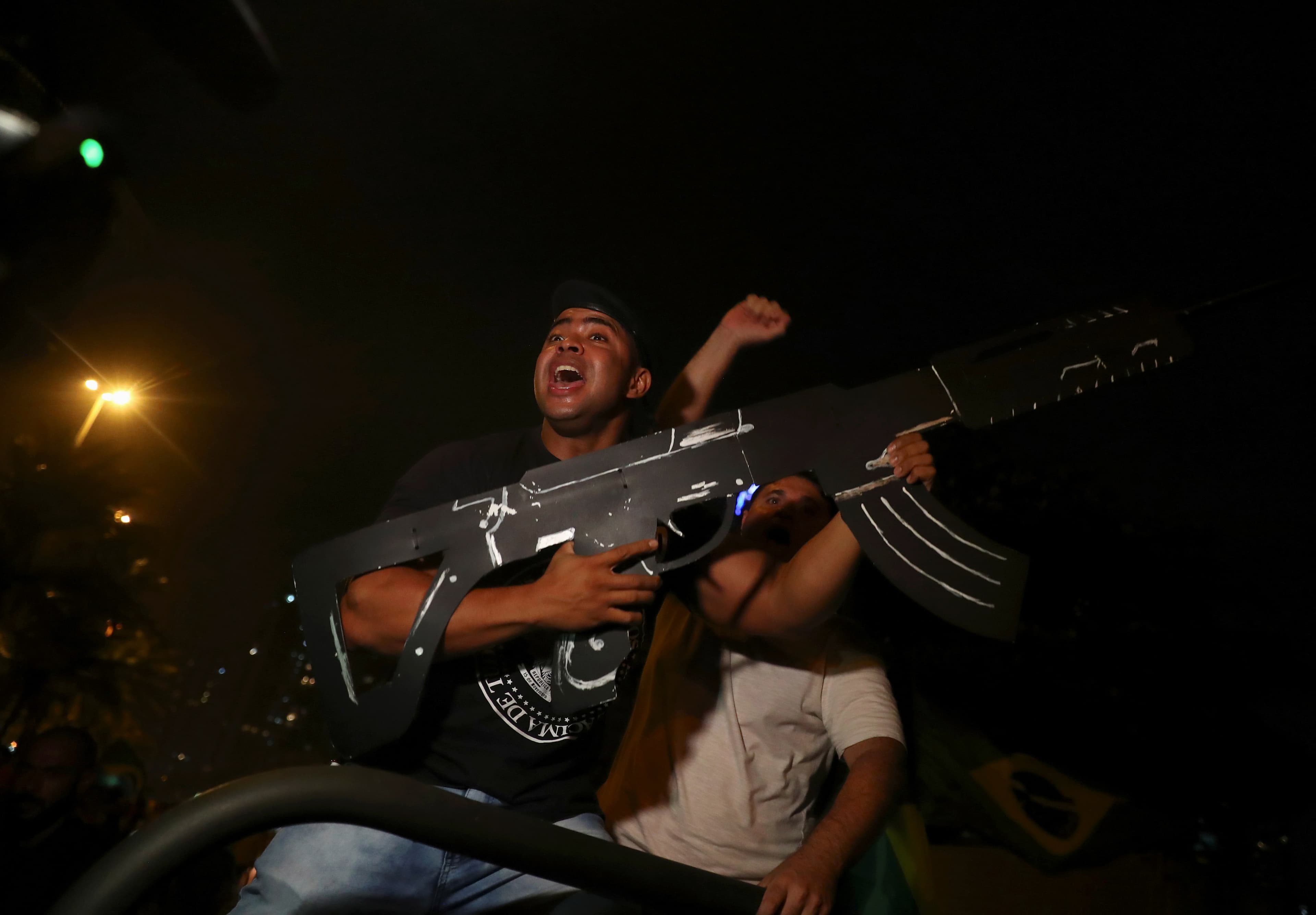 a man wearing a dark t-shirt holds a large cardboard gun