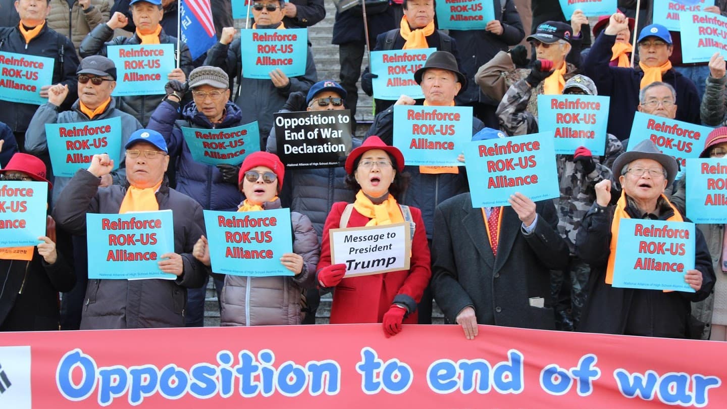 A group of protesters wear yellow scarves and hold blue signs.