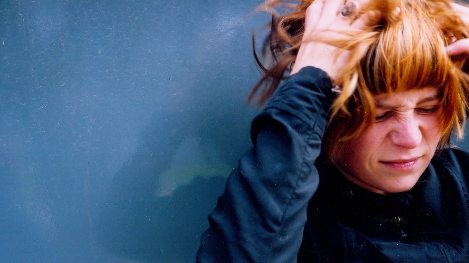 Woman with red hair grabs her head with frustrated scrunched face.