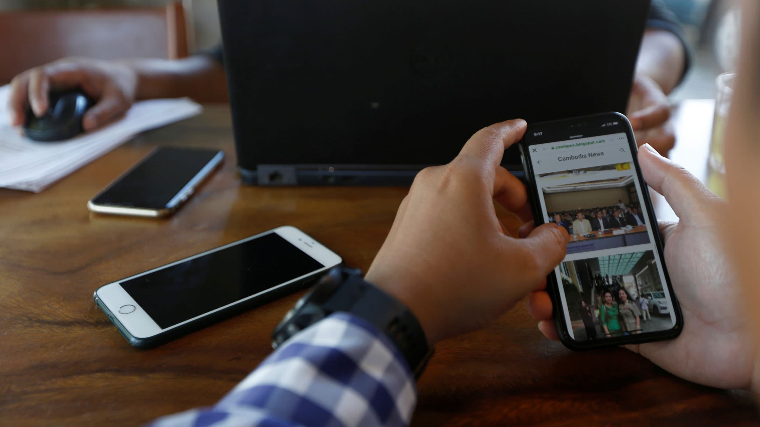 A man holds a cell phone in front of a computer screen.