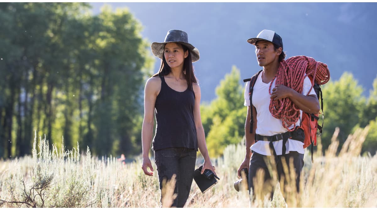 A man carrying a climbing rope stands on a field with a woman wearing a black hat.