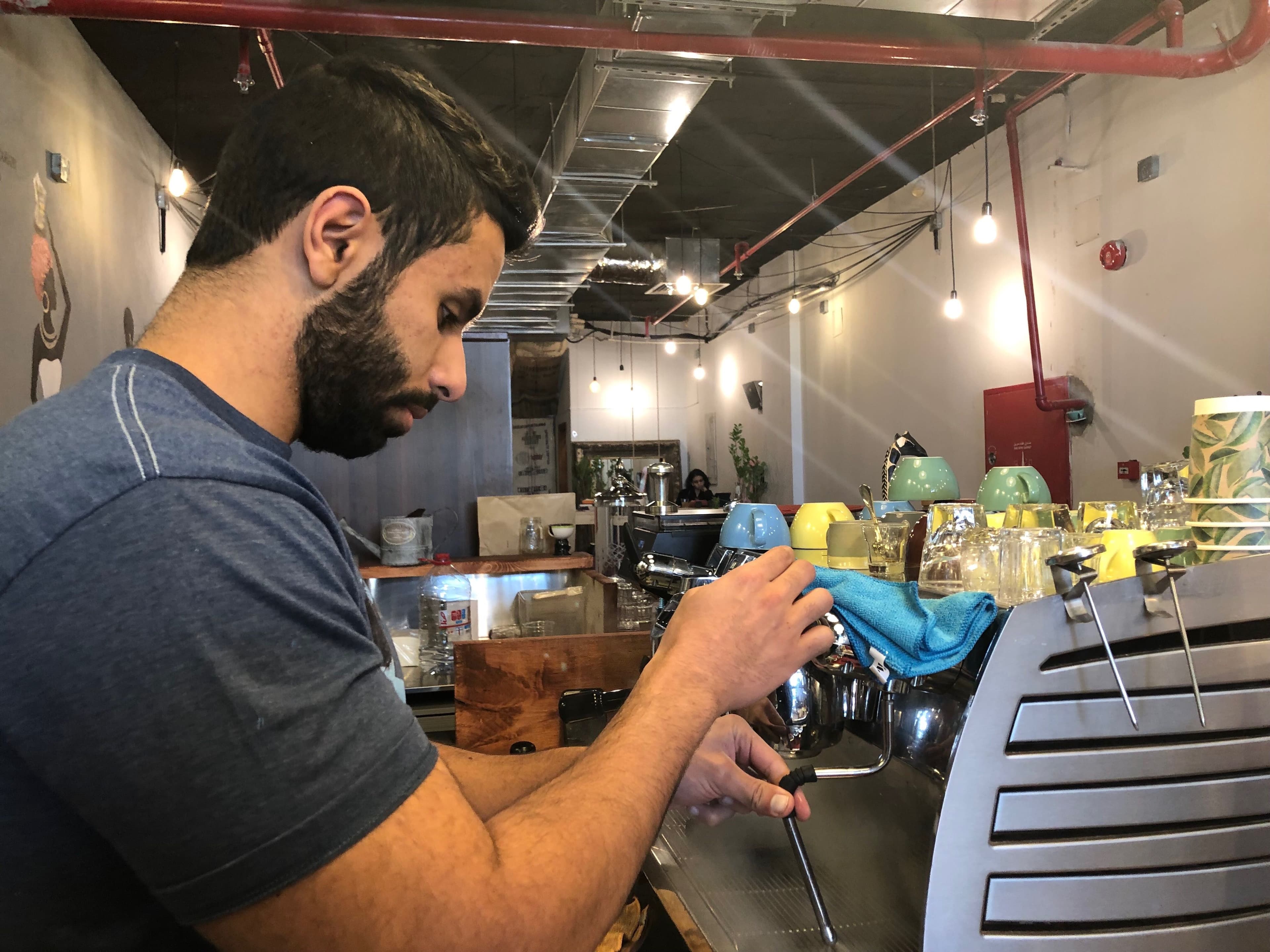 A beared man wearing a blue t-shirt works the espresso machine.