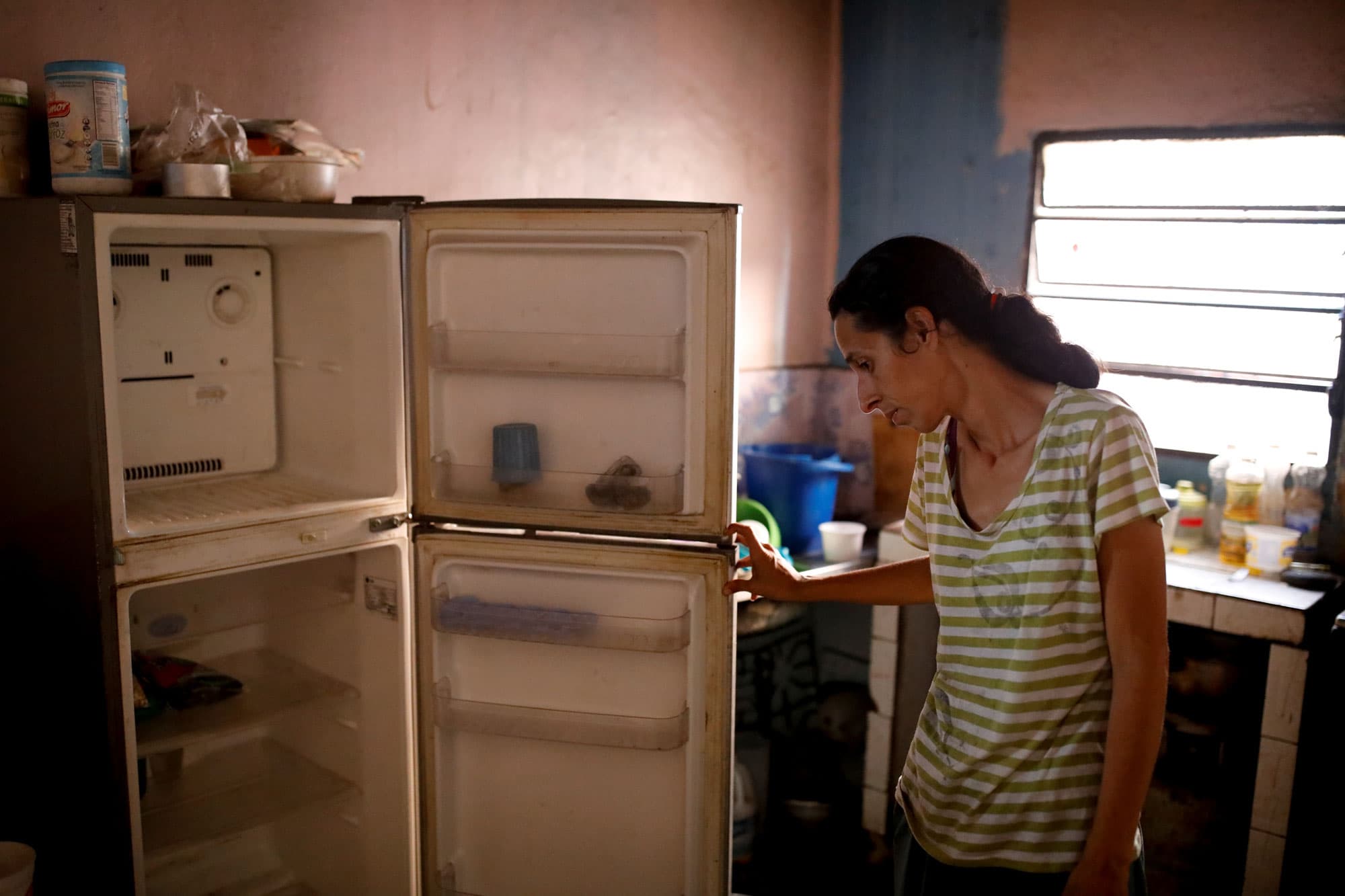 A woman is shown standing, opening up her empty refrigerator.