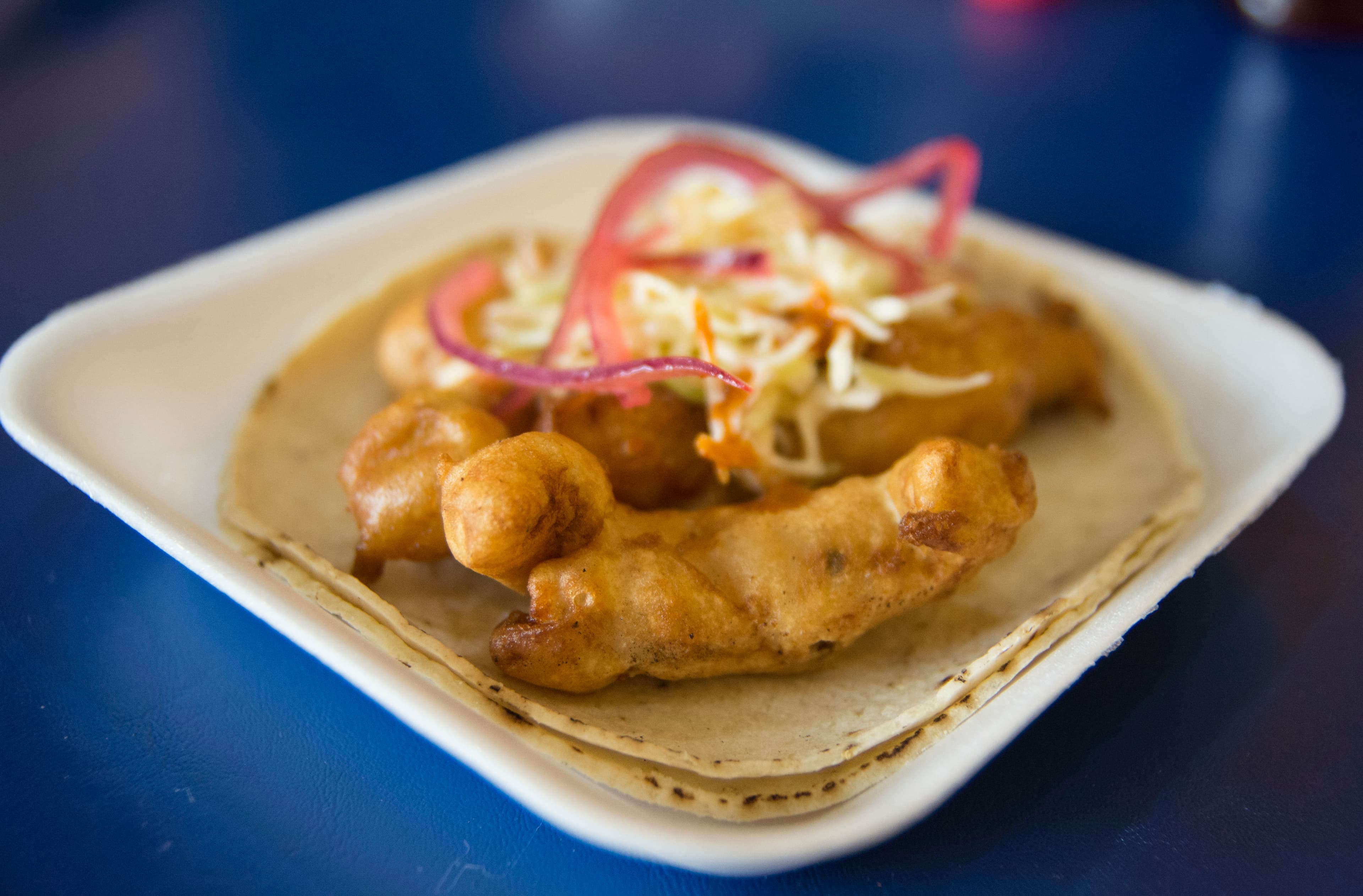 Pieces of fried fish on a tortilla on a white plate.