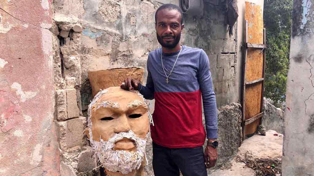 A man poses next to a large papier-mache mask
