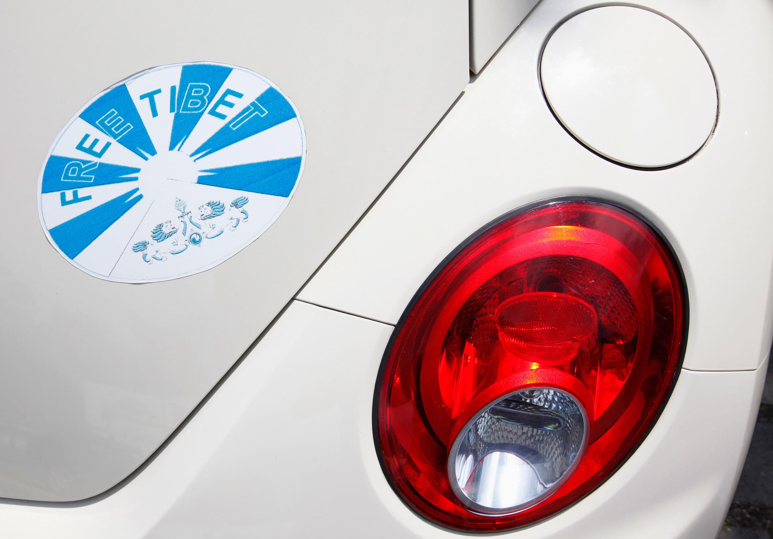 A bumper sticker on the rear of a car near the taillight says 