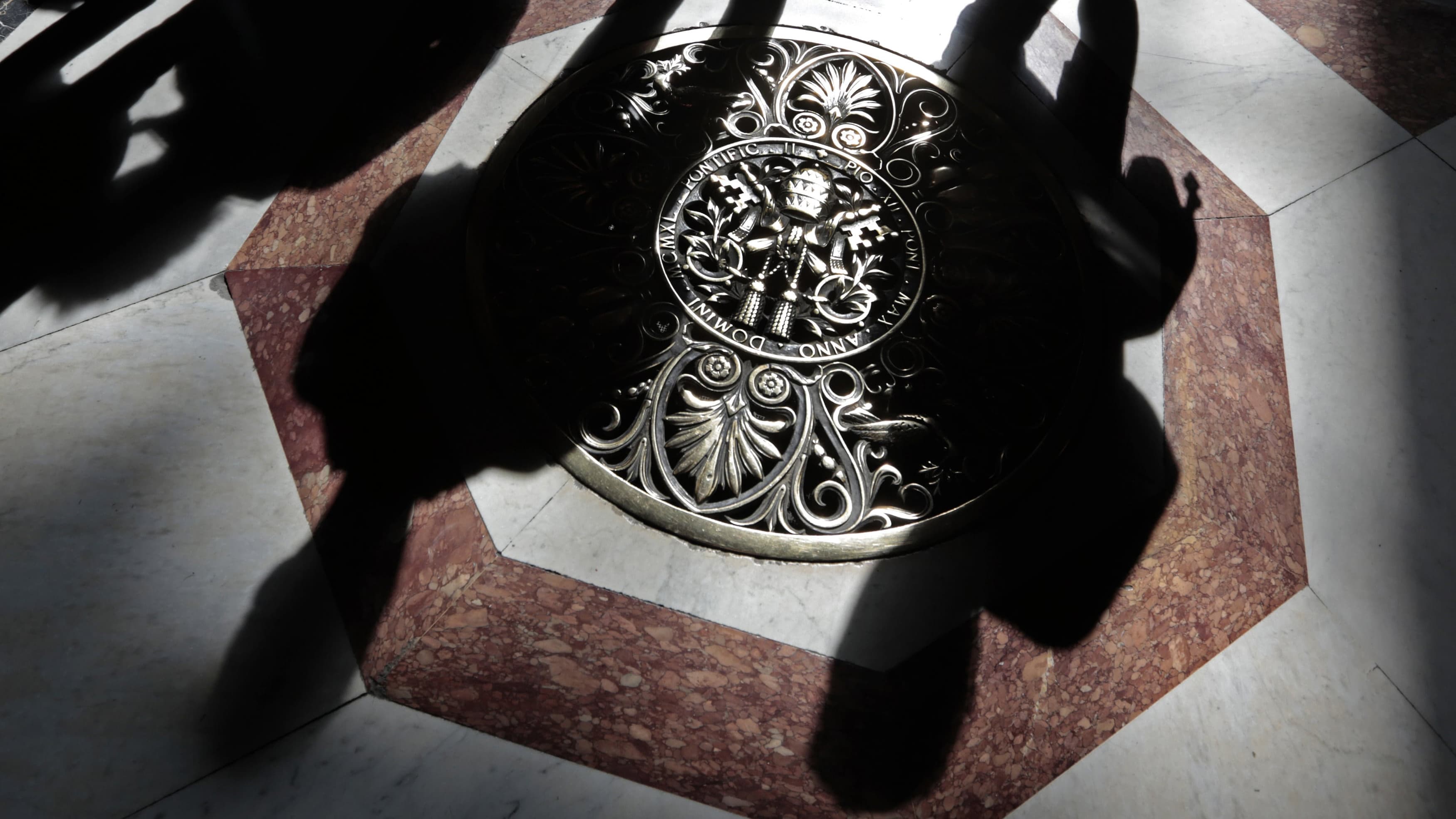 Shadows of tourists are cast across a papal crest on the floor