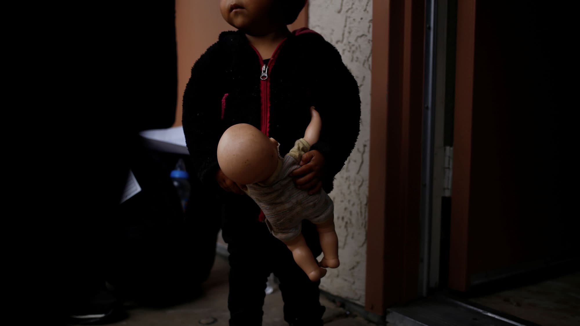 A young child is shown holding a doll by the arm.