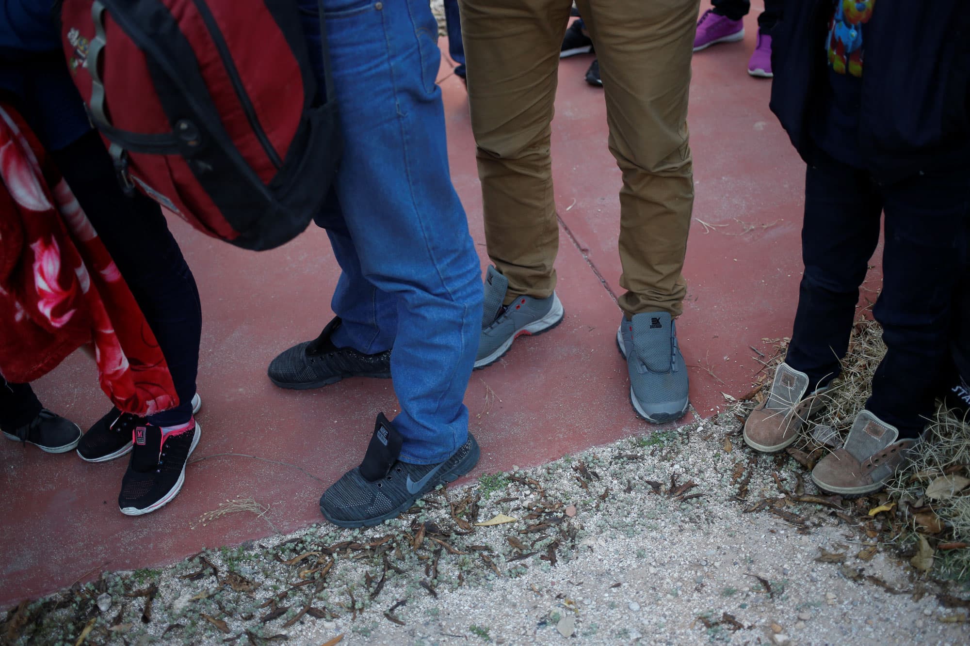 A photograph showing several people standing in line wearing shoes without laces.