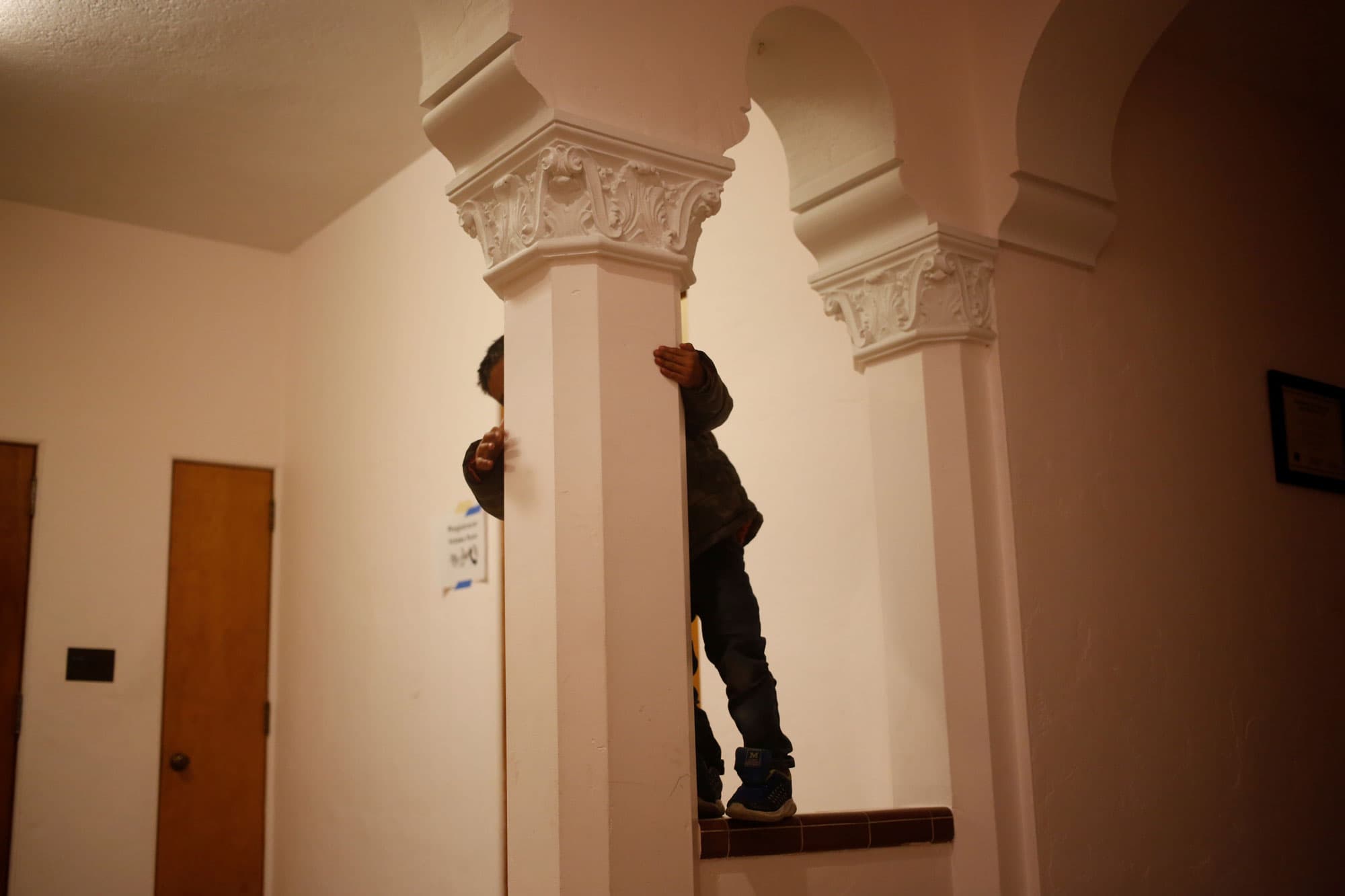A young Guatemalan boy hides behind an ornate column in a monastery.