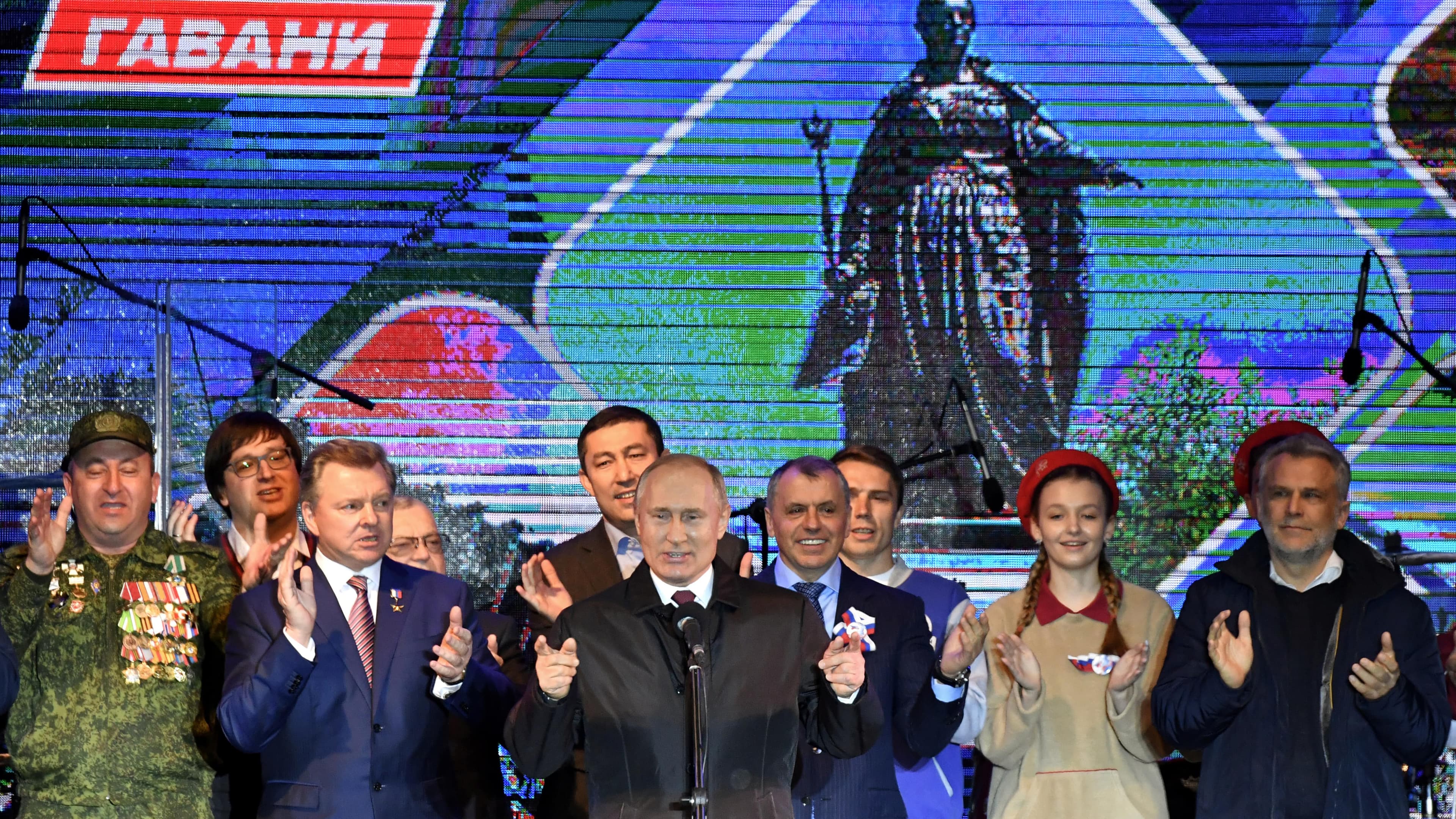 Russian President Vladimir Putin stands on a stage surrounded by others