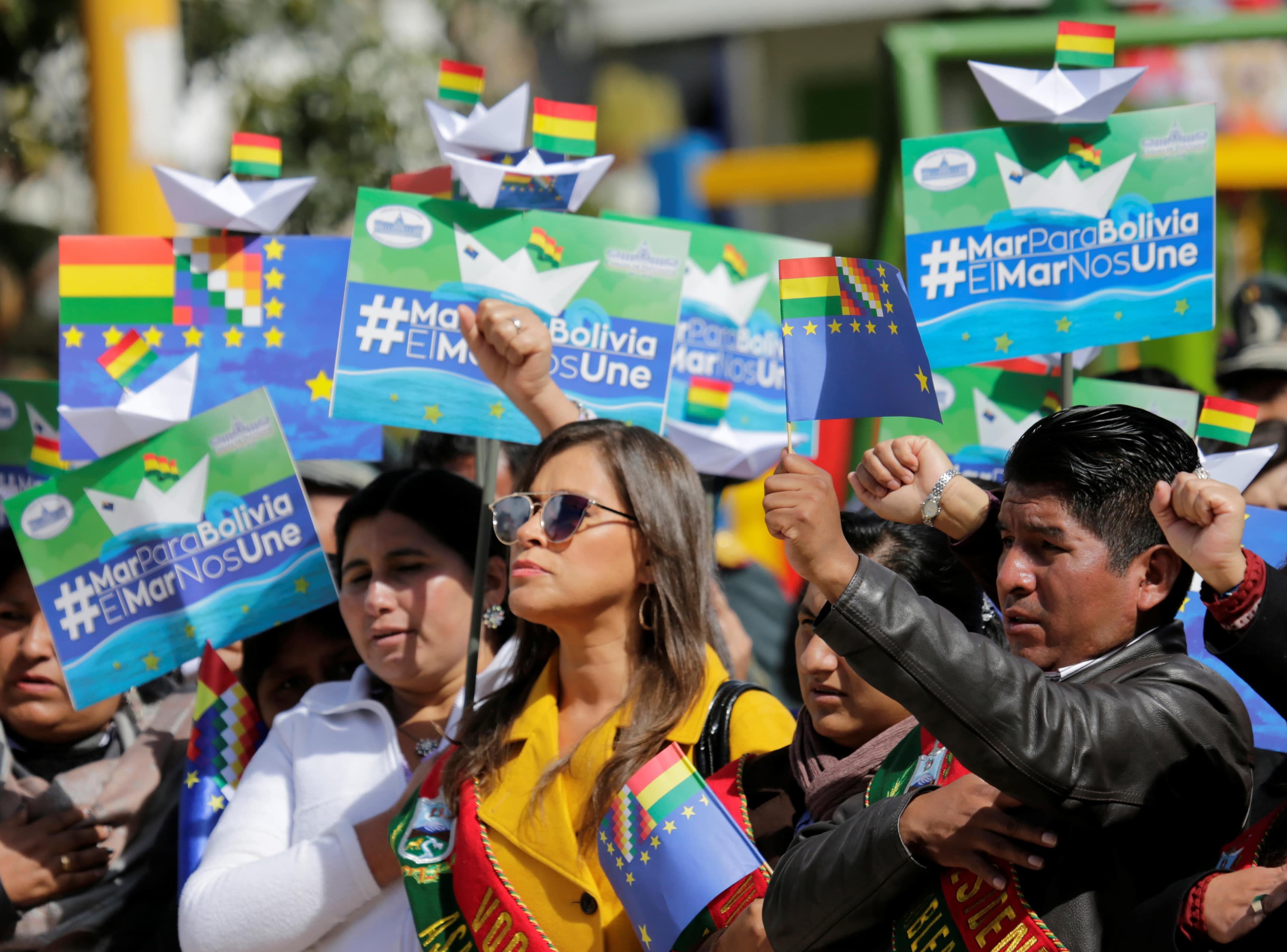 several people are seen demonstrating and holding signs that read "Sea for Bolivia, Sea unit us."