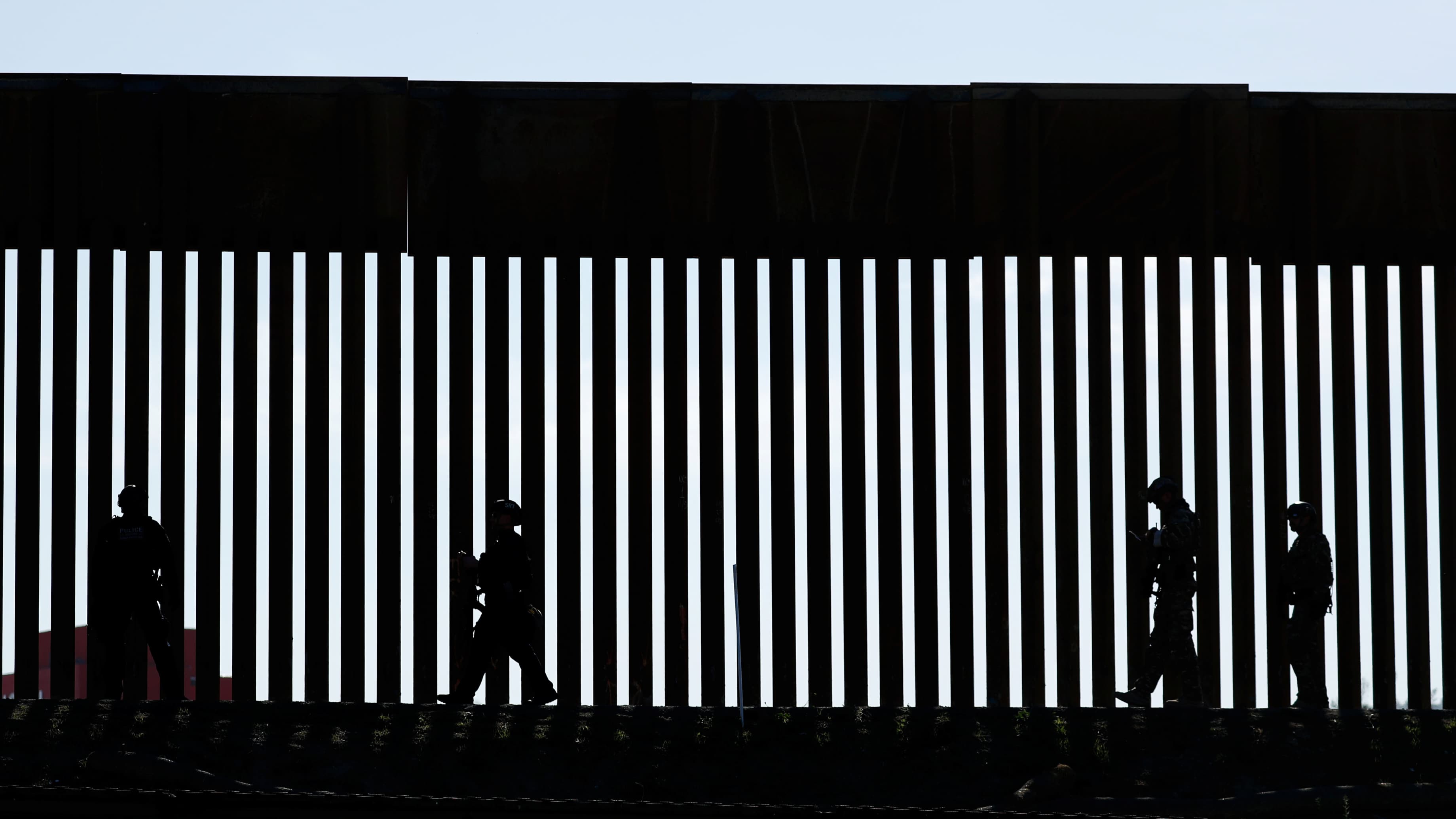 Shadow of patrolmen along slated wall at US border.