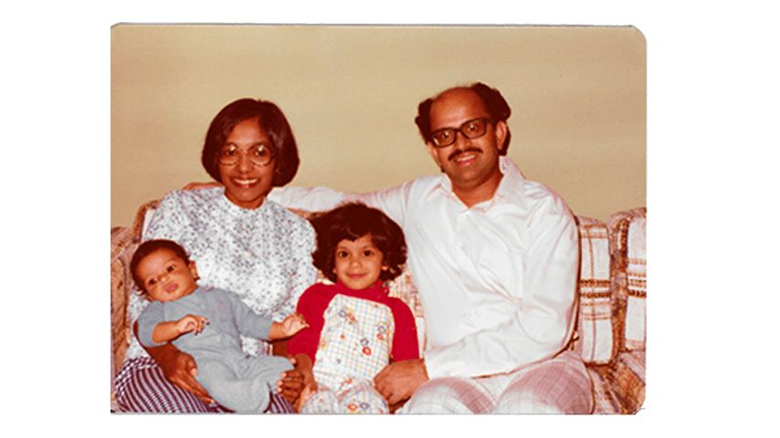 A mother holds a baby and a child sits between the mother and father on a couch.