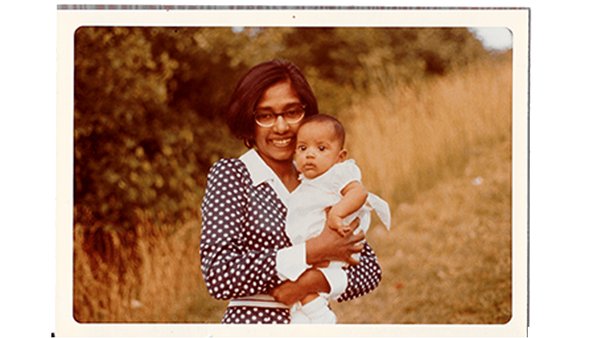 A mother holds a baby and smiles for the camera.