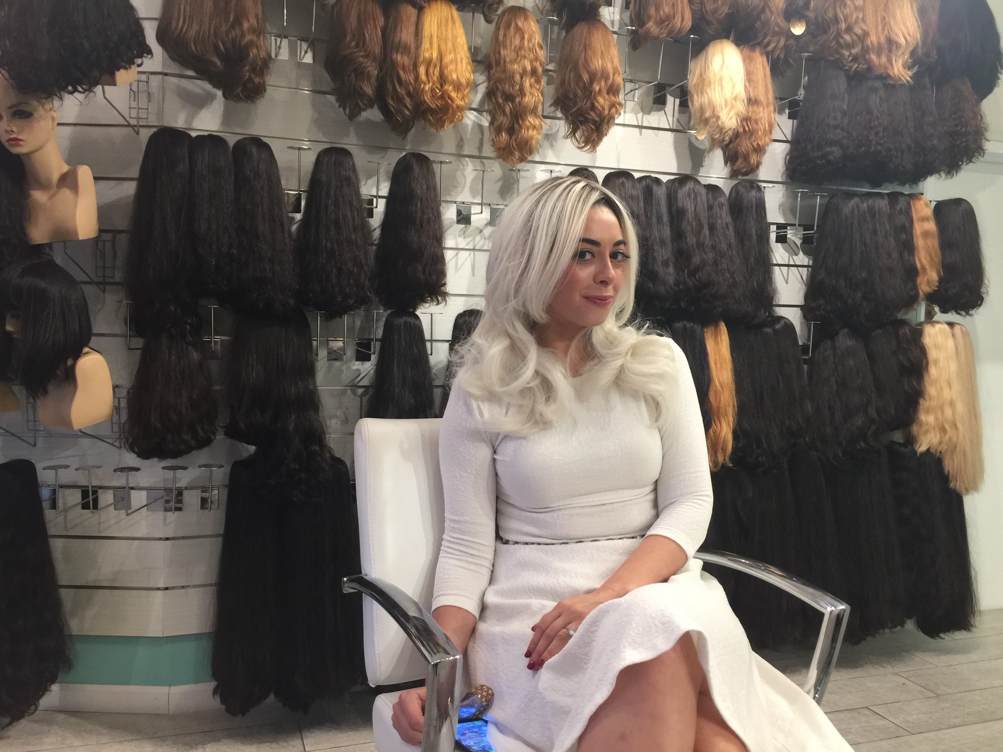 Woman with light blond wig and wearing all white sits in a chair.
