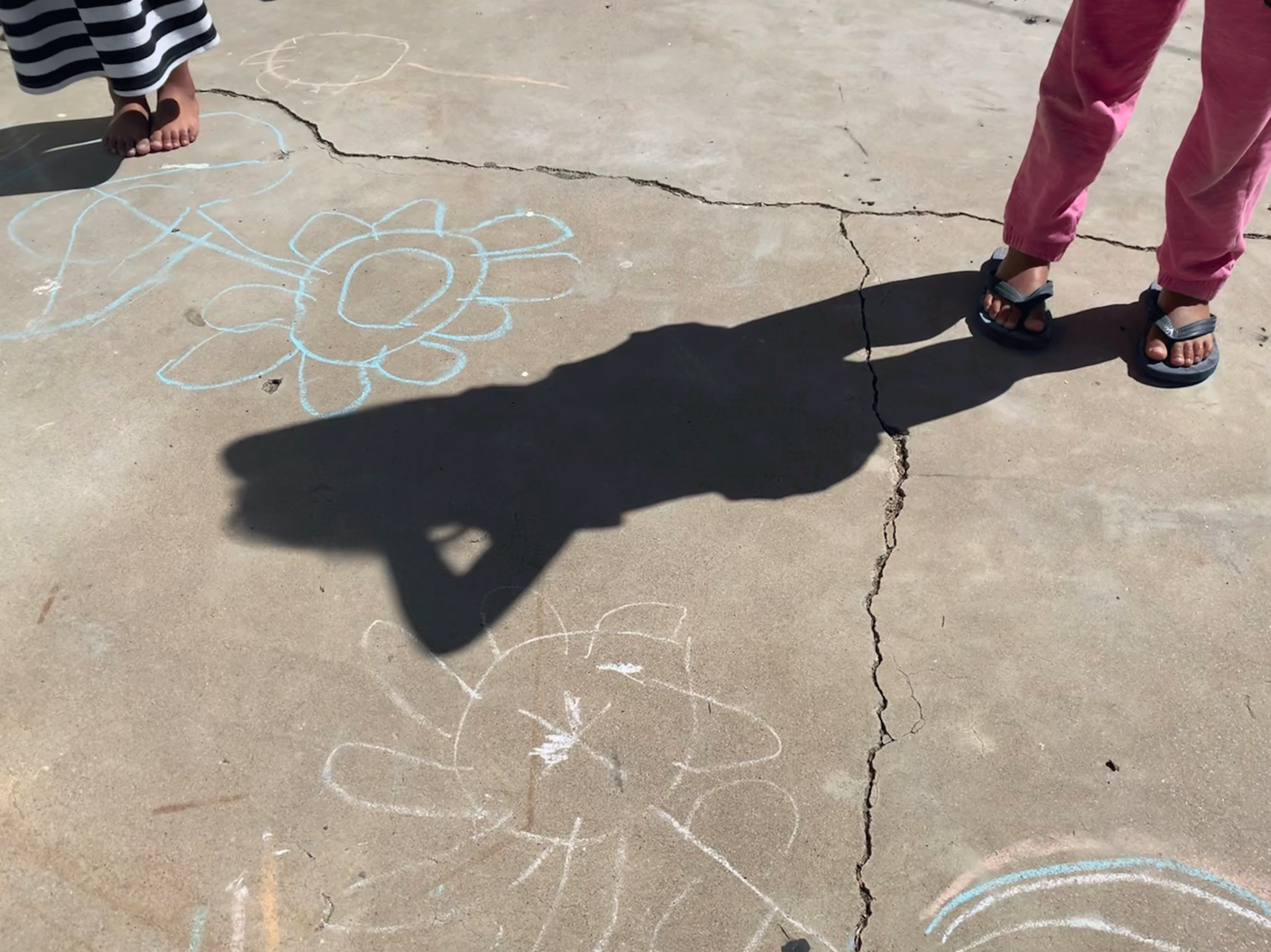 a shadow of a girl and two pairs of feet over chalk drawings.