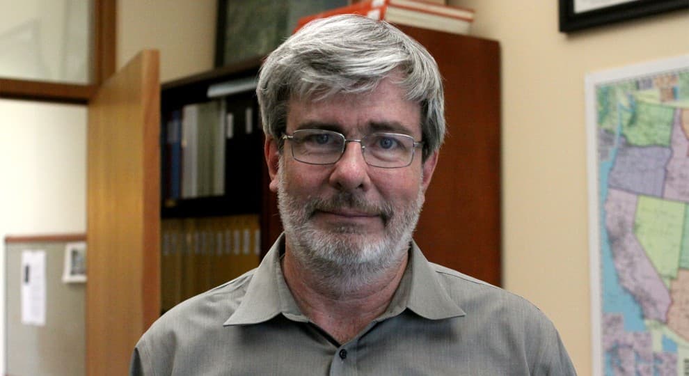 A man with a beard and glasses looks at the camera