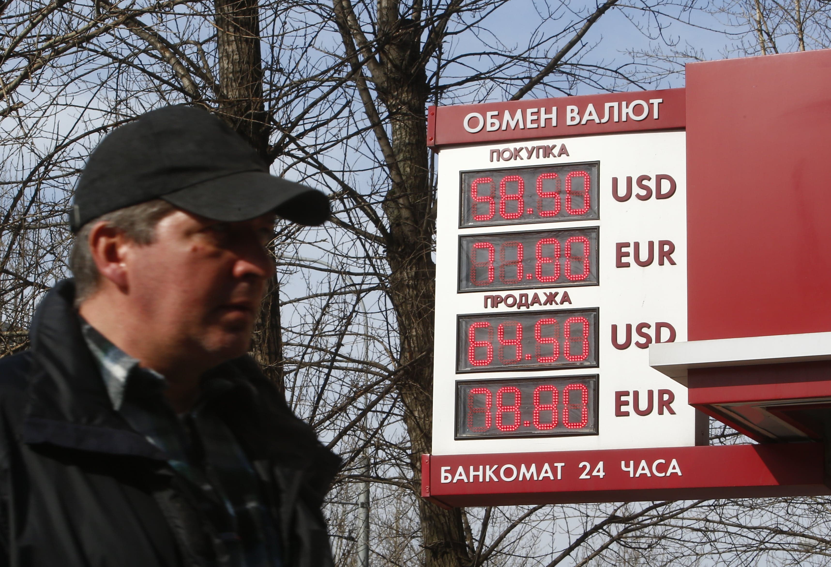 a man walks past a currency exchange rate board