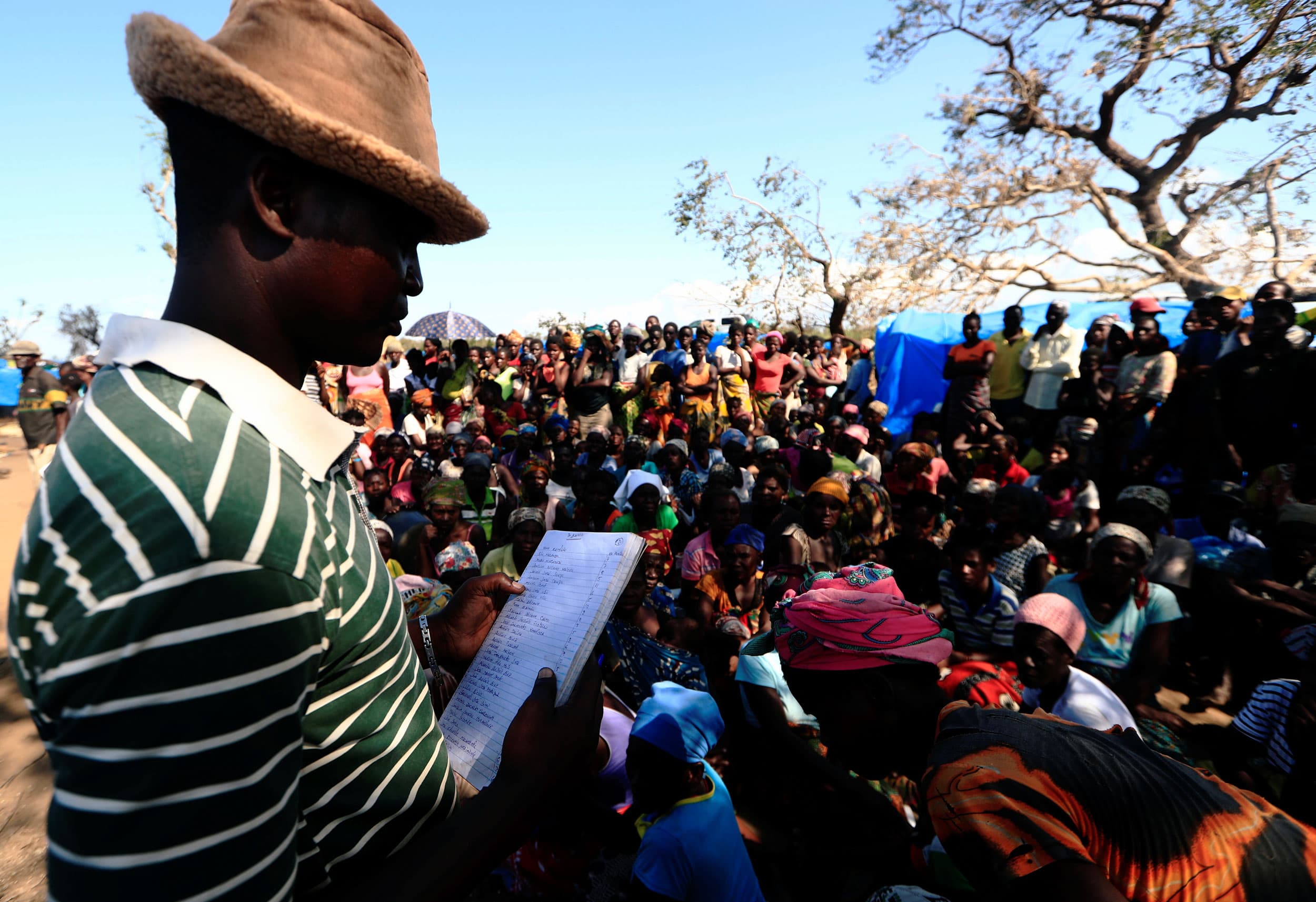A man holds a piece of paper with a list. Dozens of people surround him.