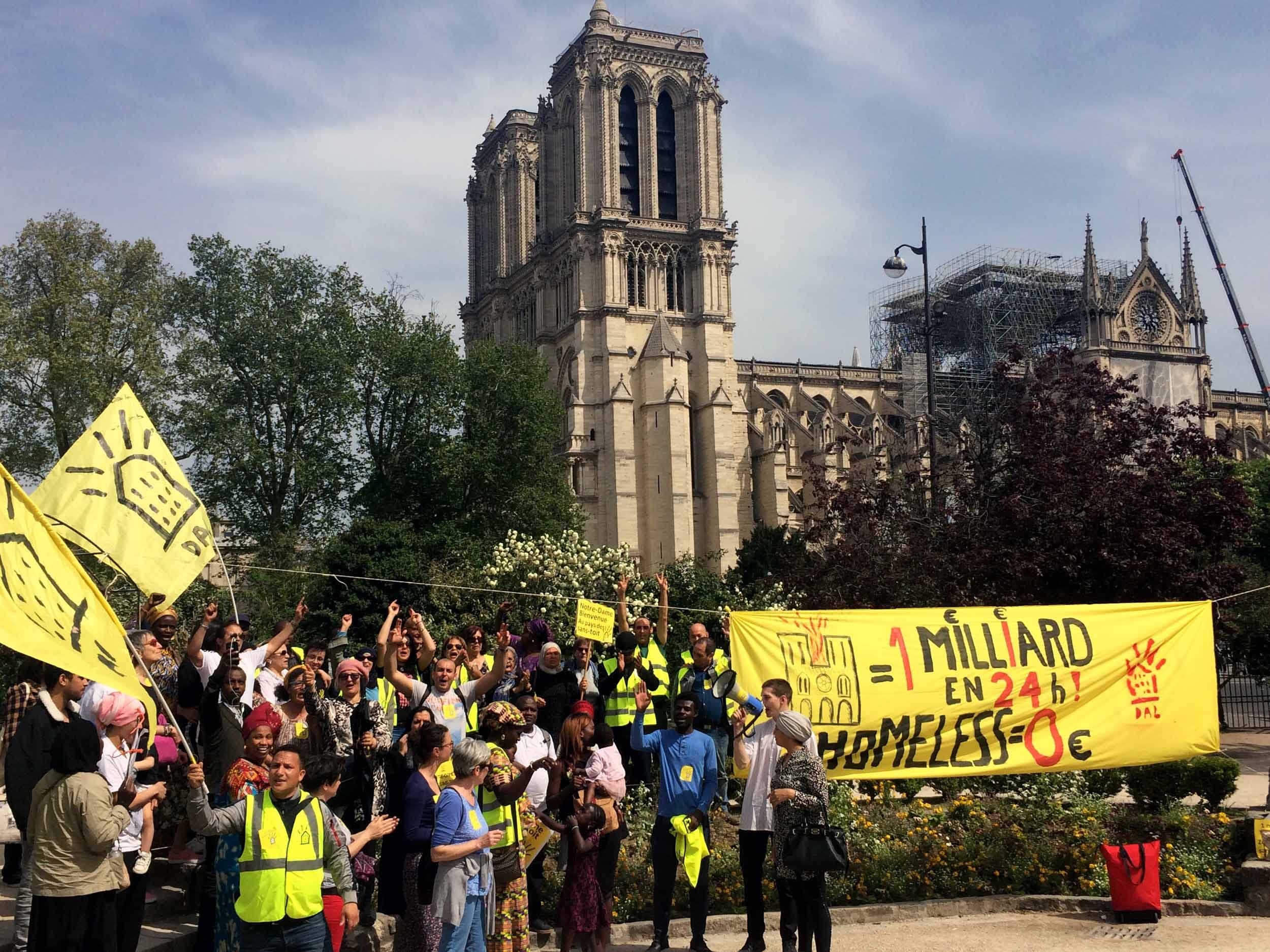 A crowd of people hold yellow signs and a banner. The towers of Notre-Dame are visible in the background.
