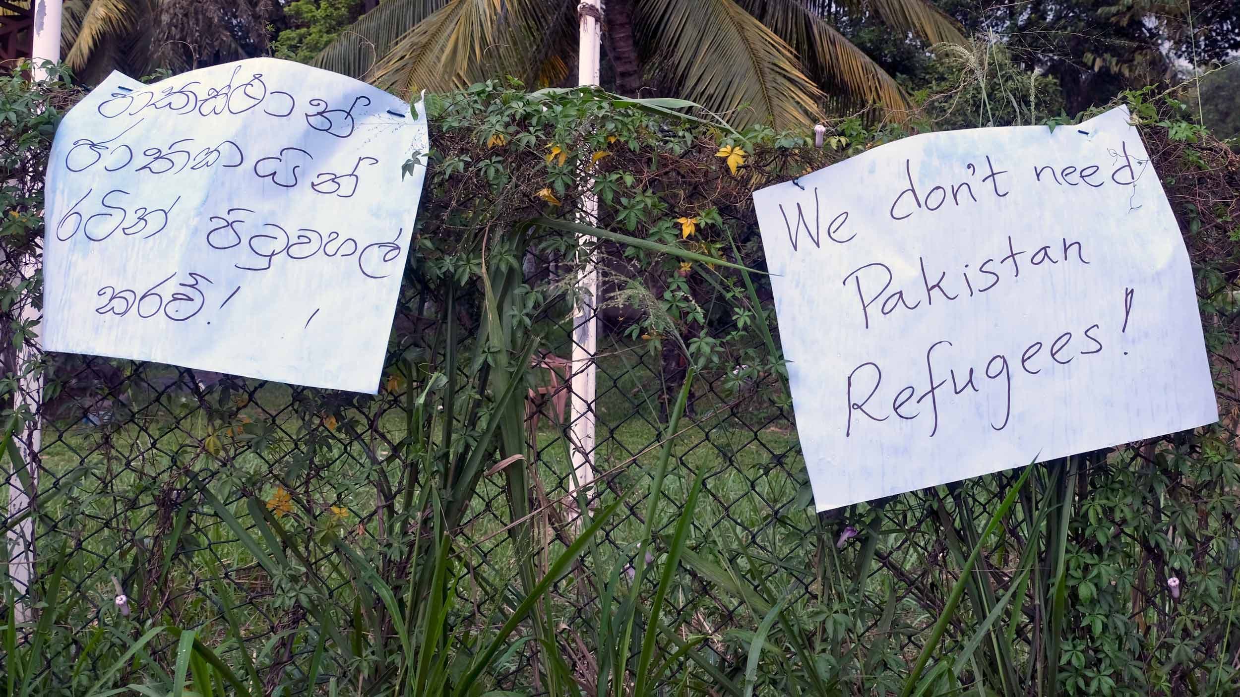 Signs hang over a fence. Once says 
