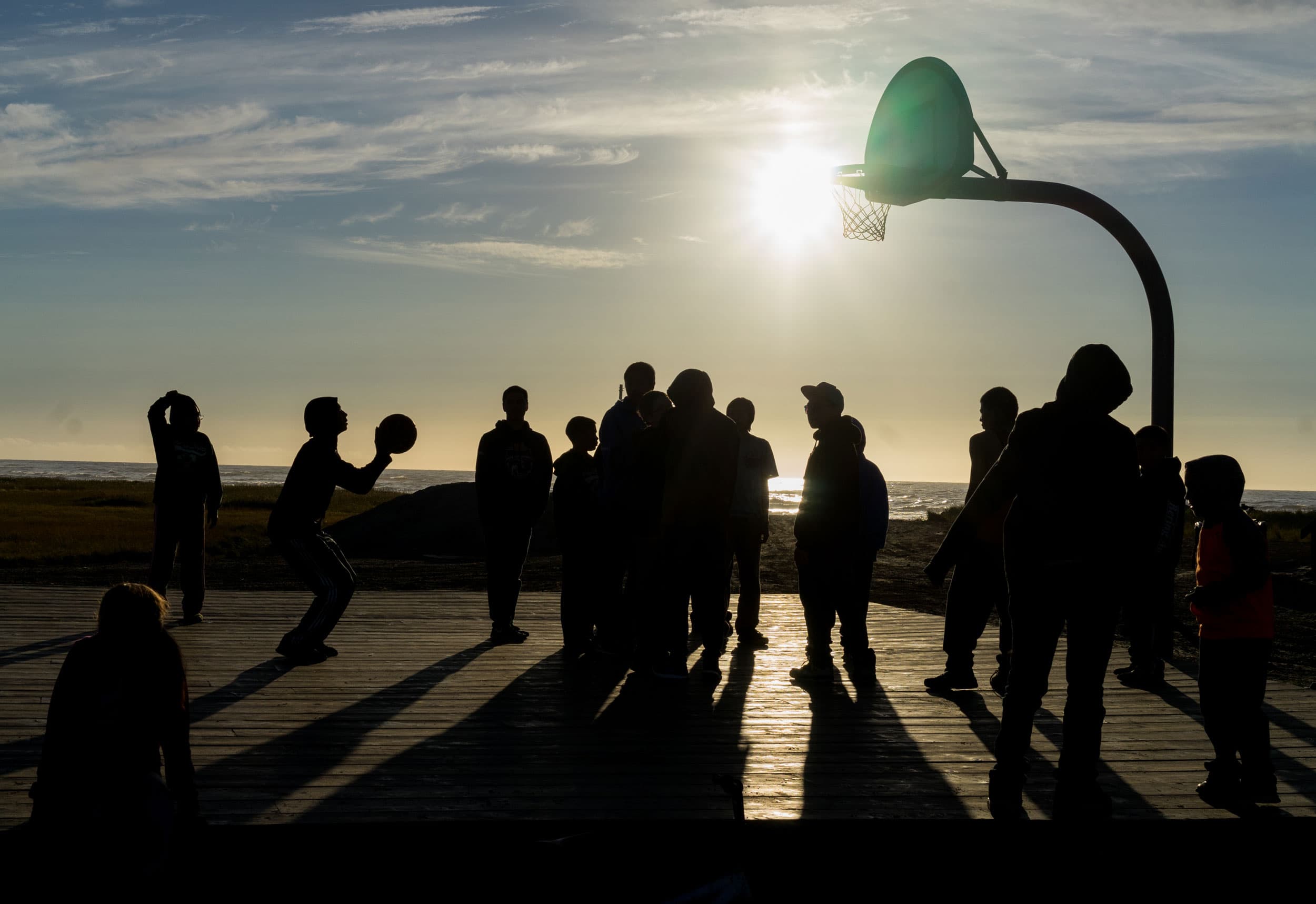 Children are silhouetted against the setting sun as they play basketball.