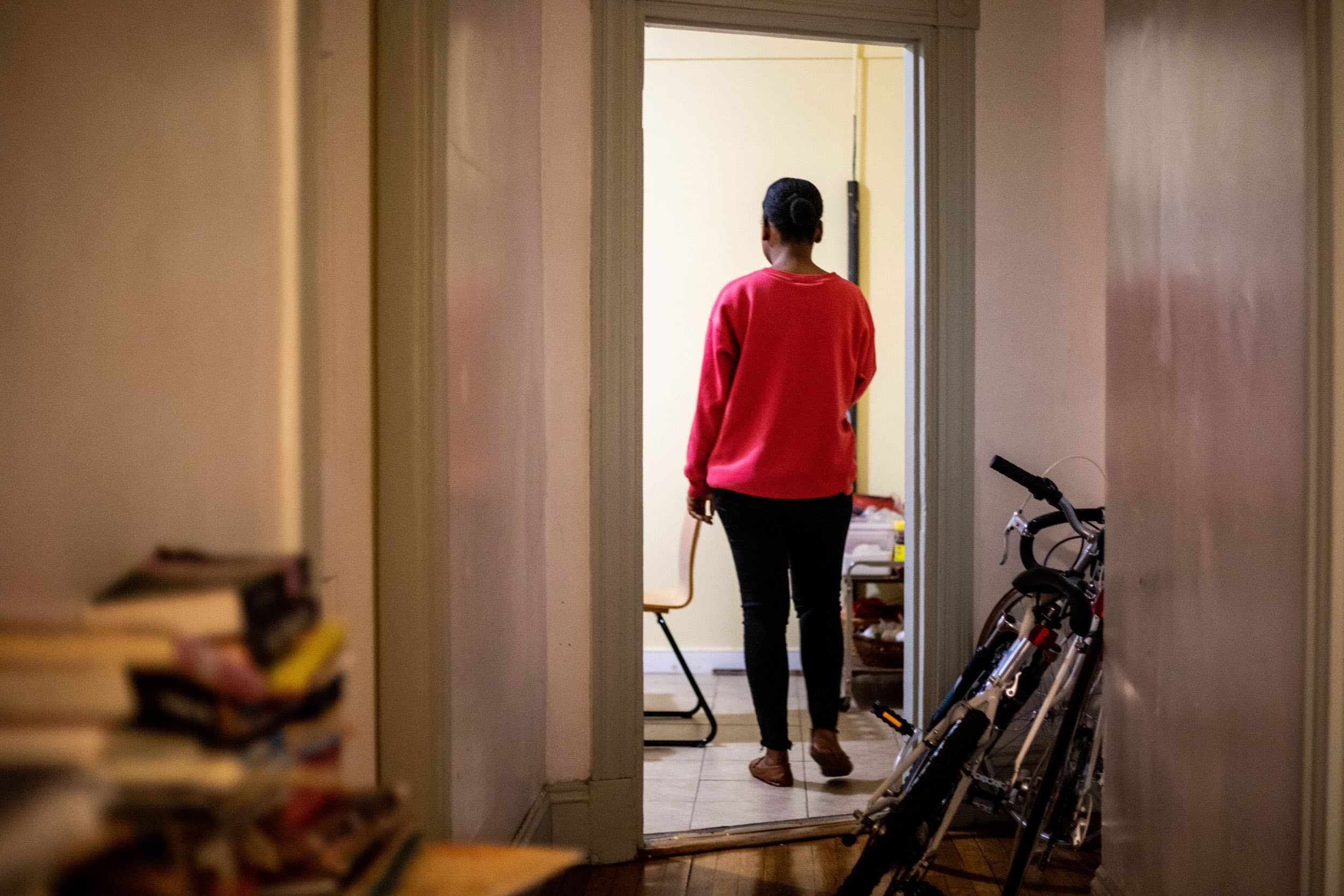 A woman is show in her kitchen with a red sweatshirt and black pants.