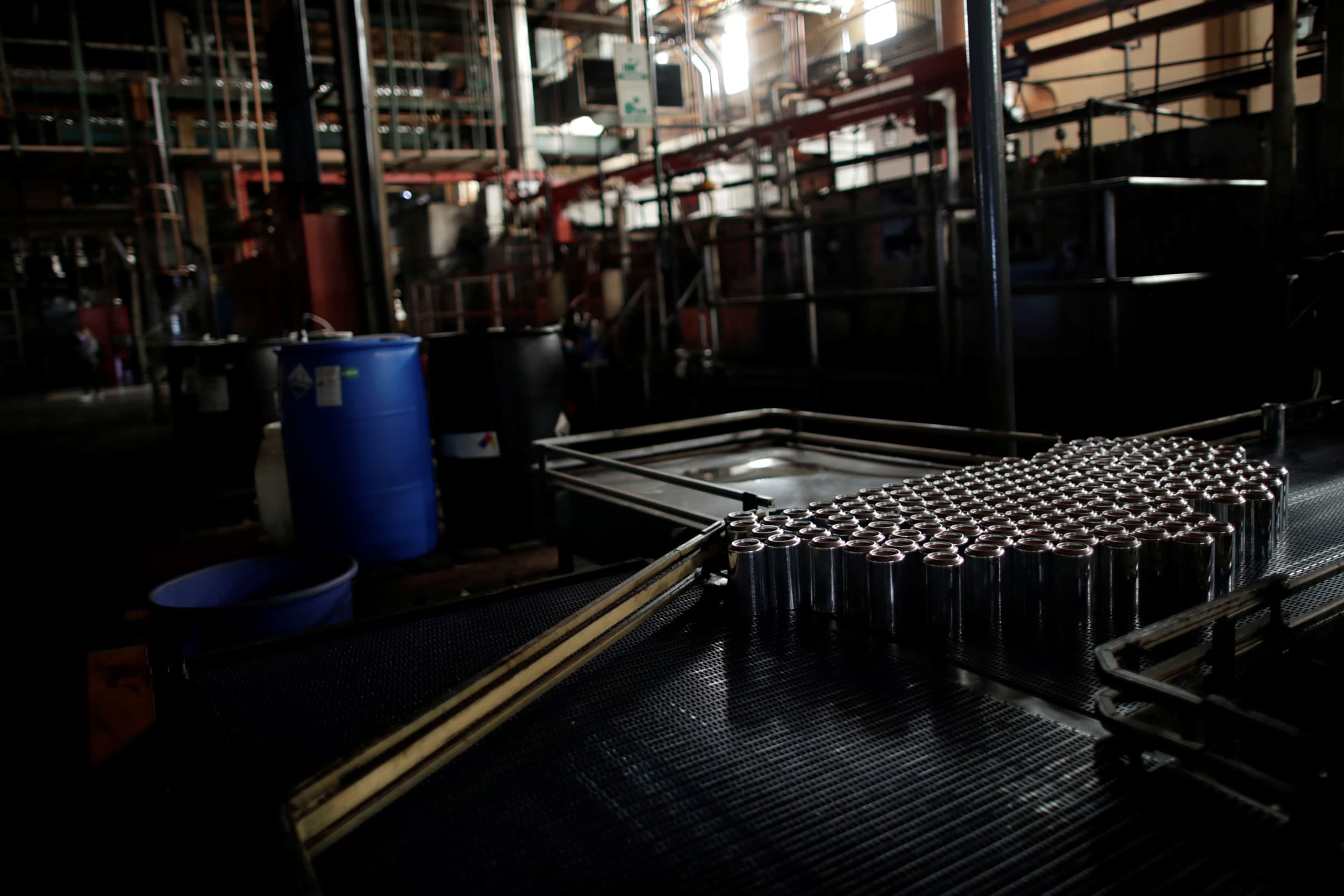 Shiny silver cans are seen on a halted machine in a darked room.