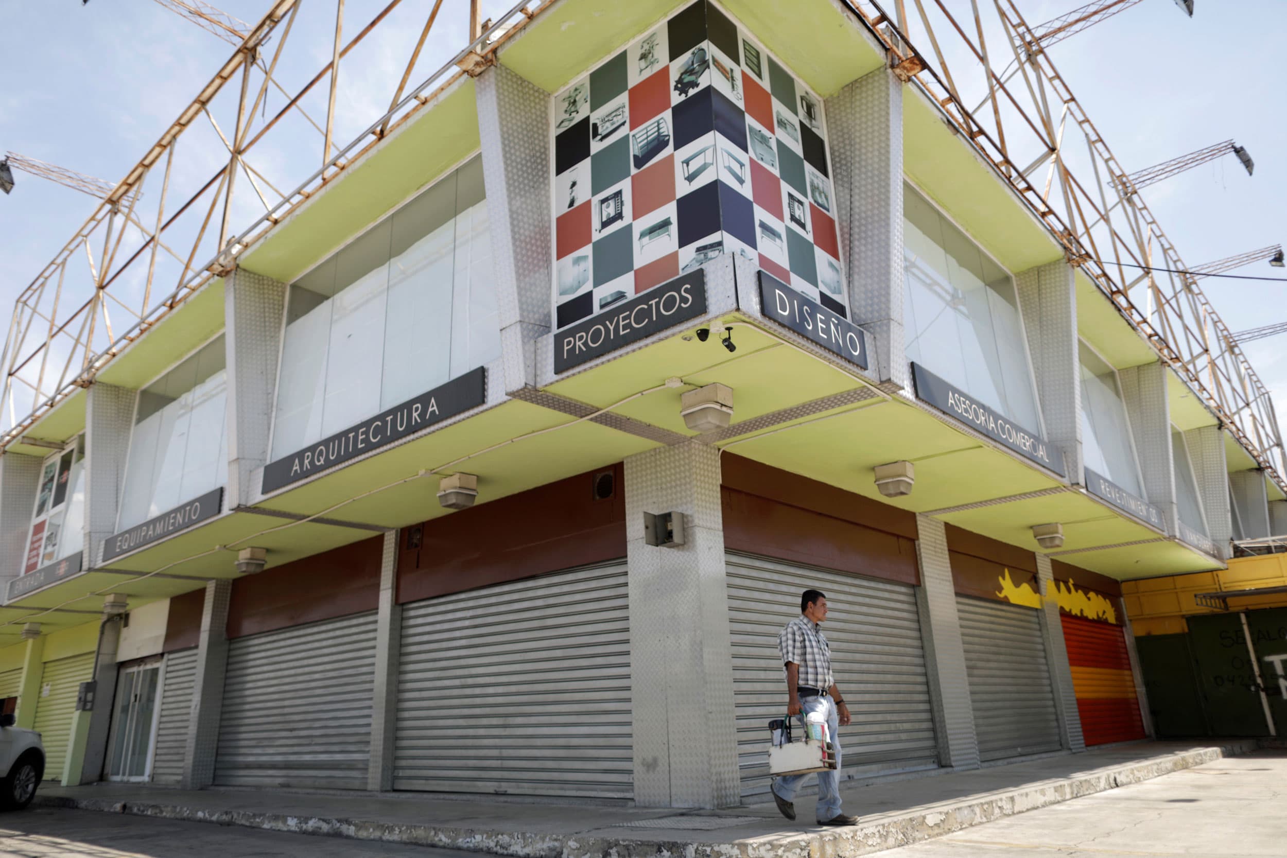 A man walks past several storefronts that have metal gates pulled down.
