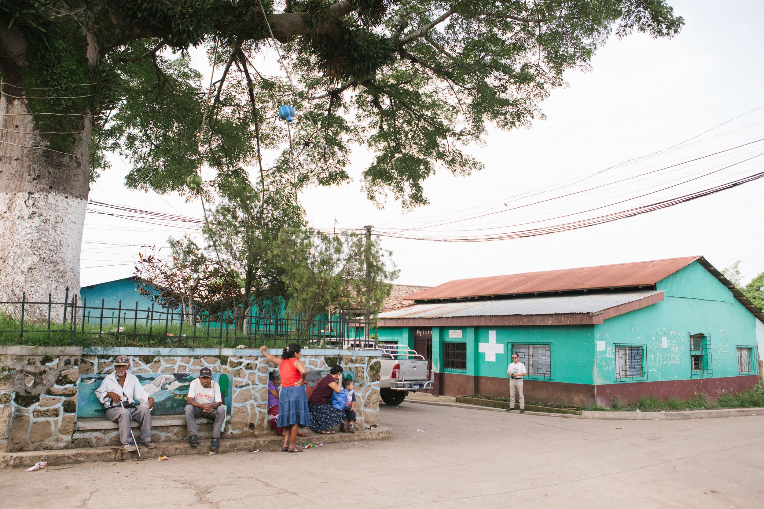 Several people are shown standing and some sitting next to a stone wall.