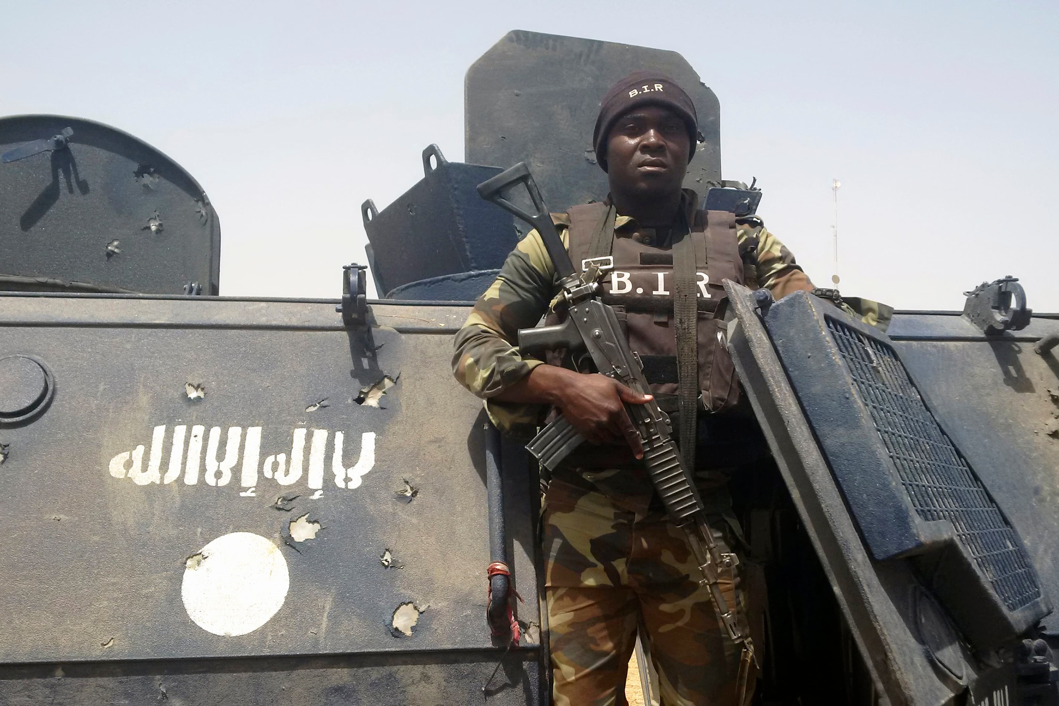 Cameroonian soldier stands near tank with Boko Haram logo on it.