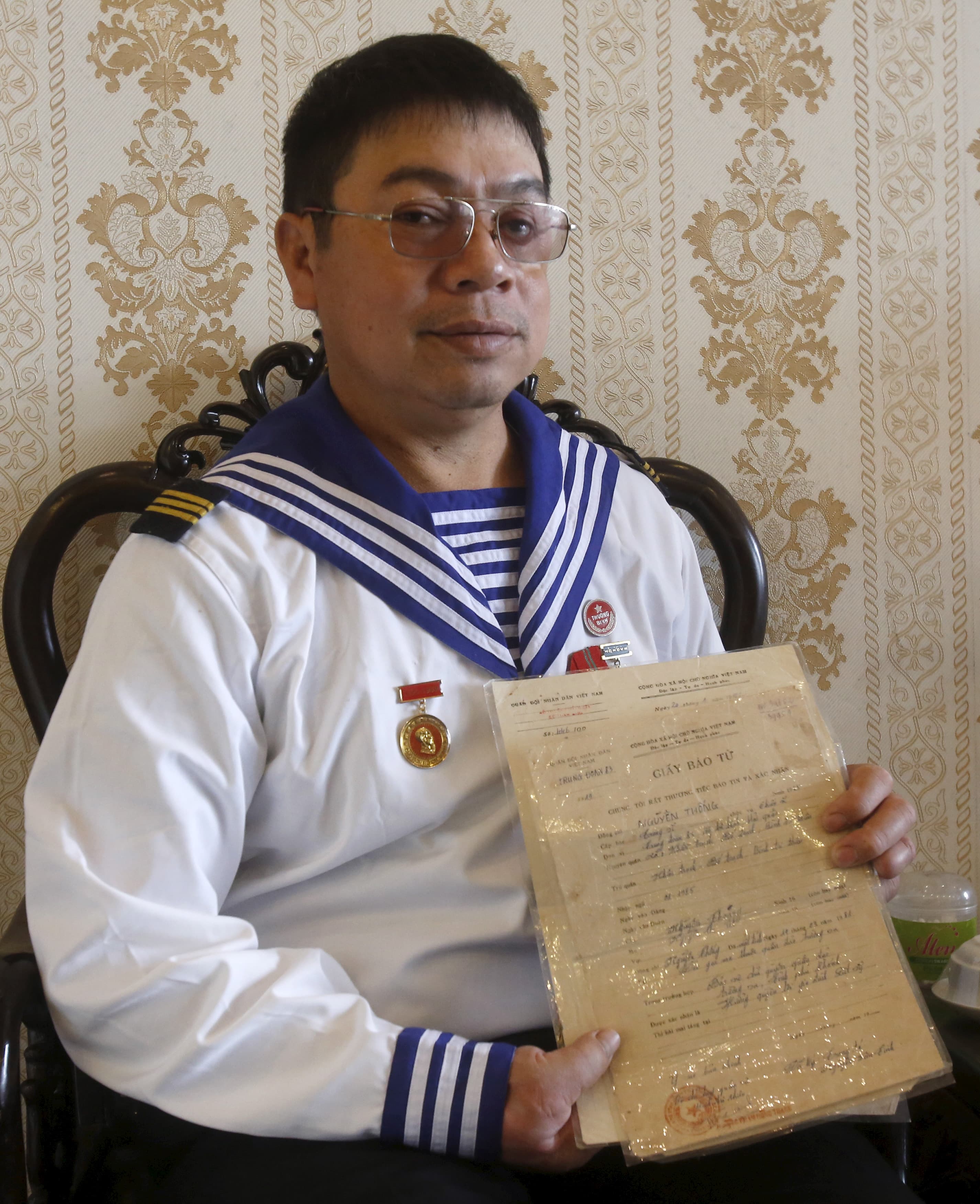 Man wears navy uniform and holds his own death certificate papers.
