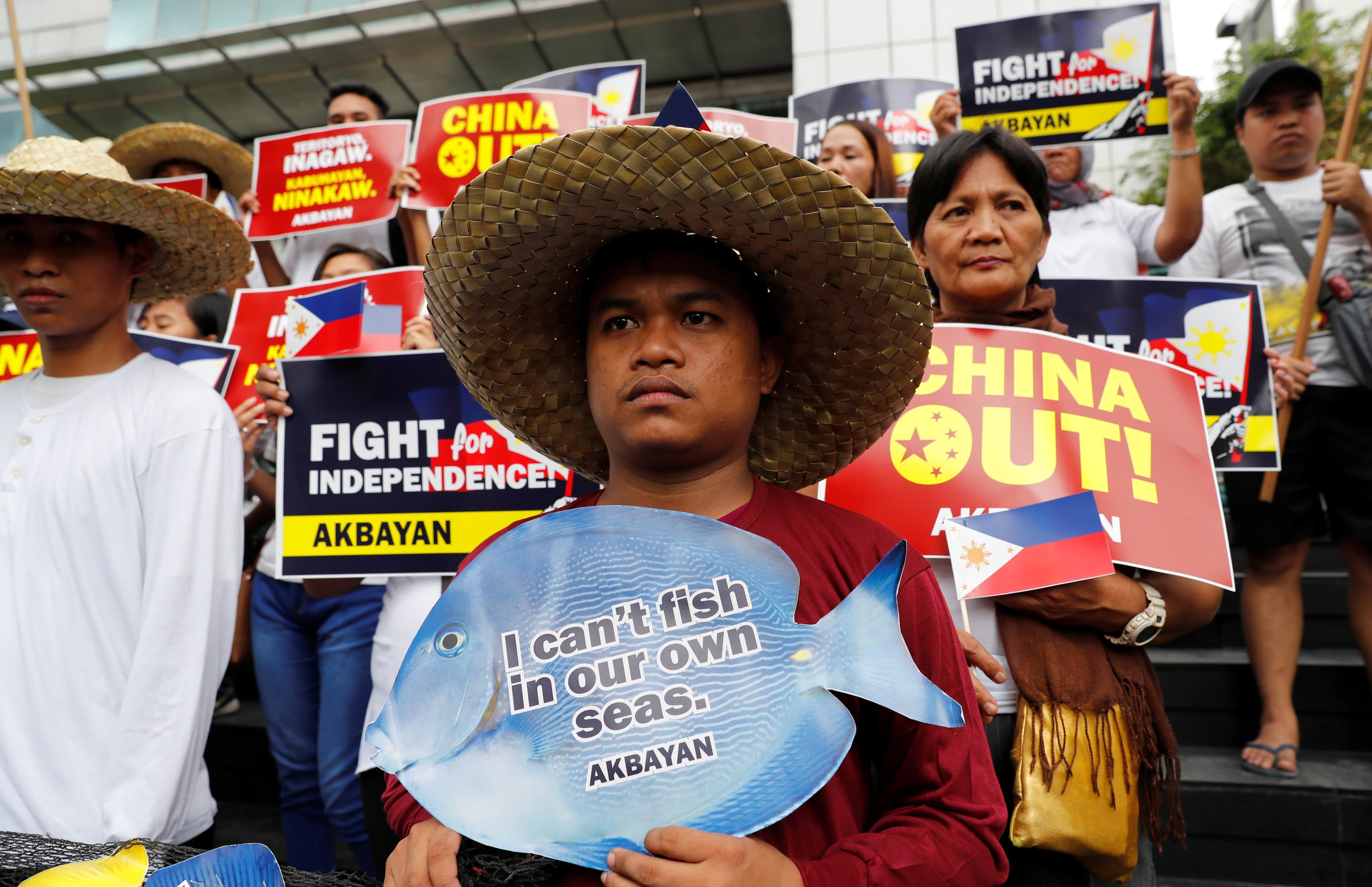 Man wearing straw fishing hat carries sign that says 