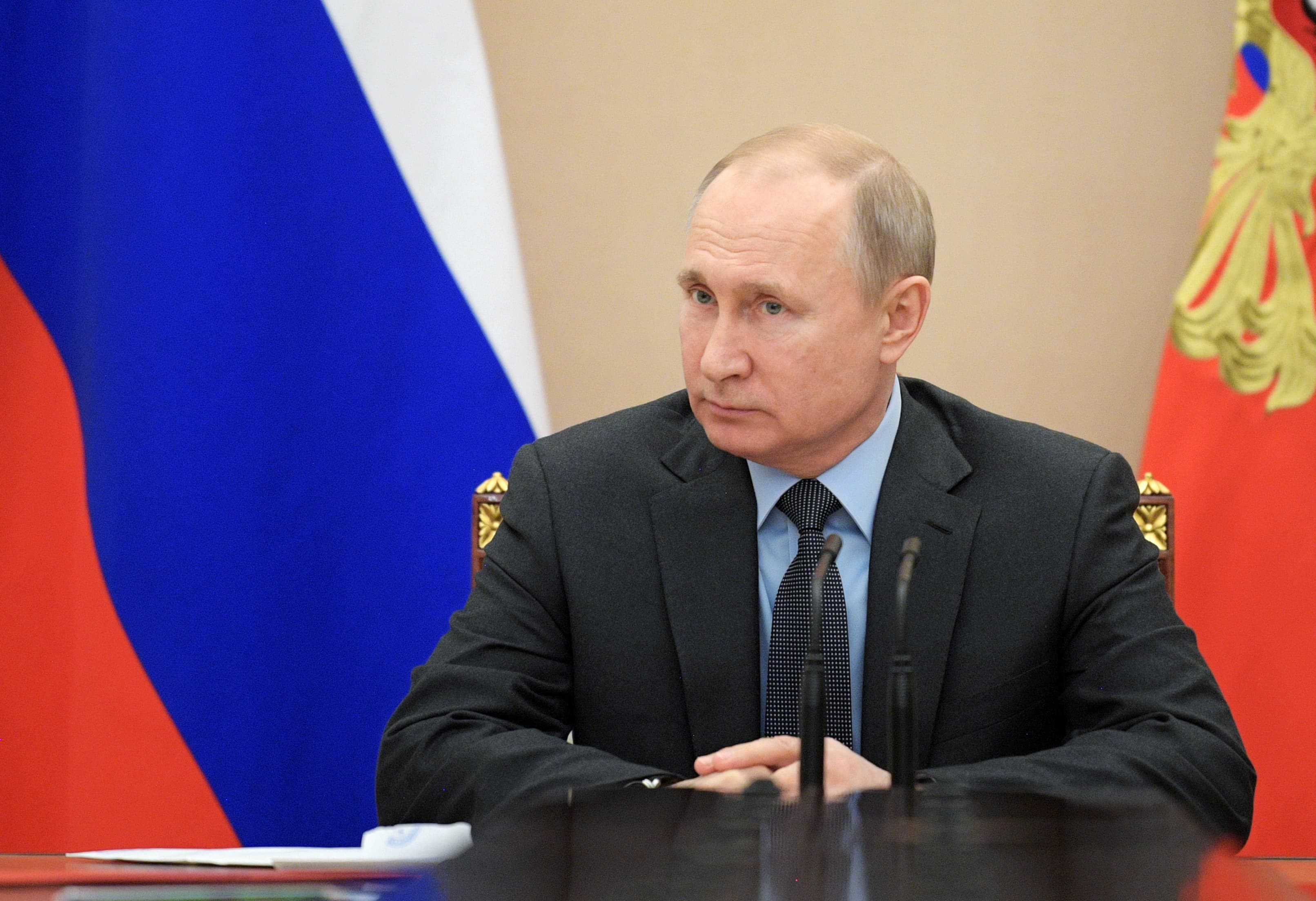 Vladimir Putin sits at a desk with the Russian flag behind him.