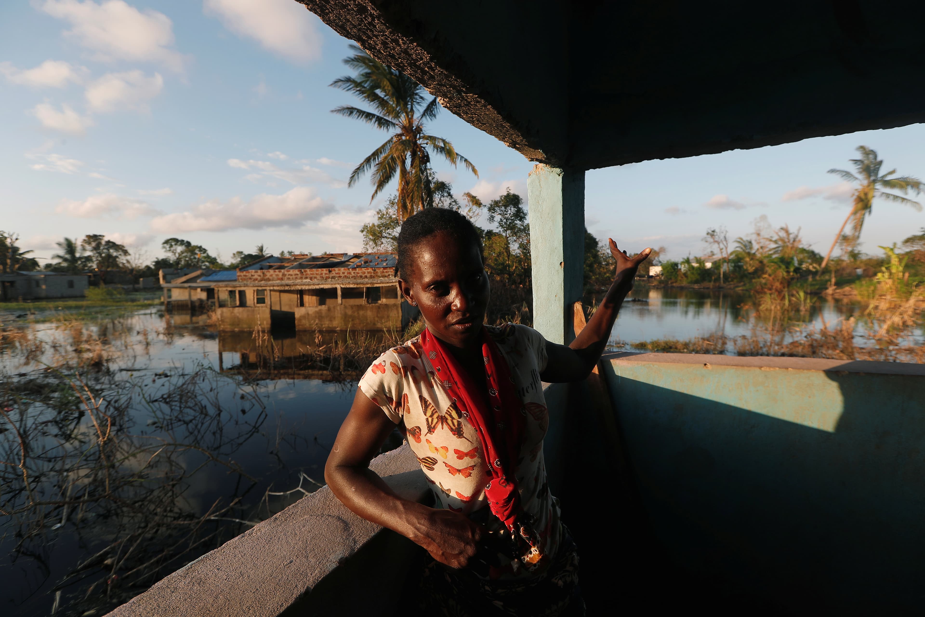 A woman stands near the corner of a house next to a flooded field.
