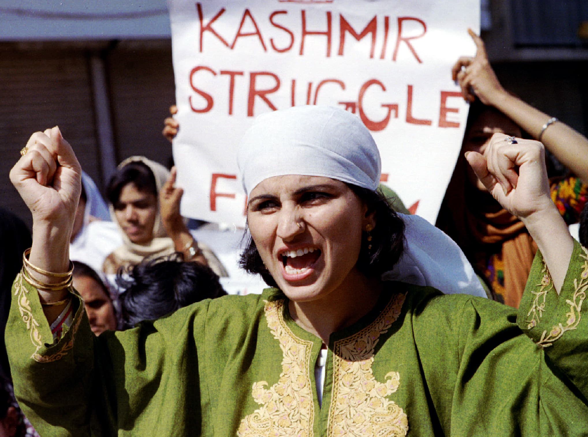 Woman in green shouts in front of Kashmir struggle sign.