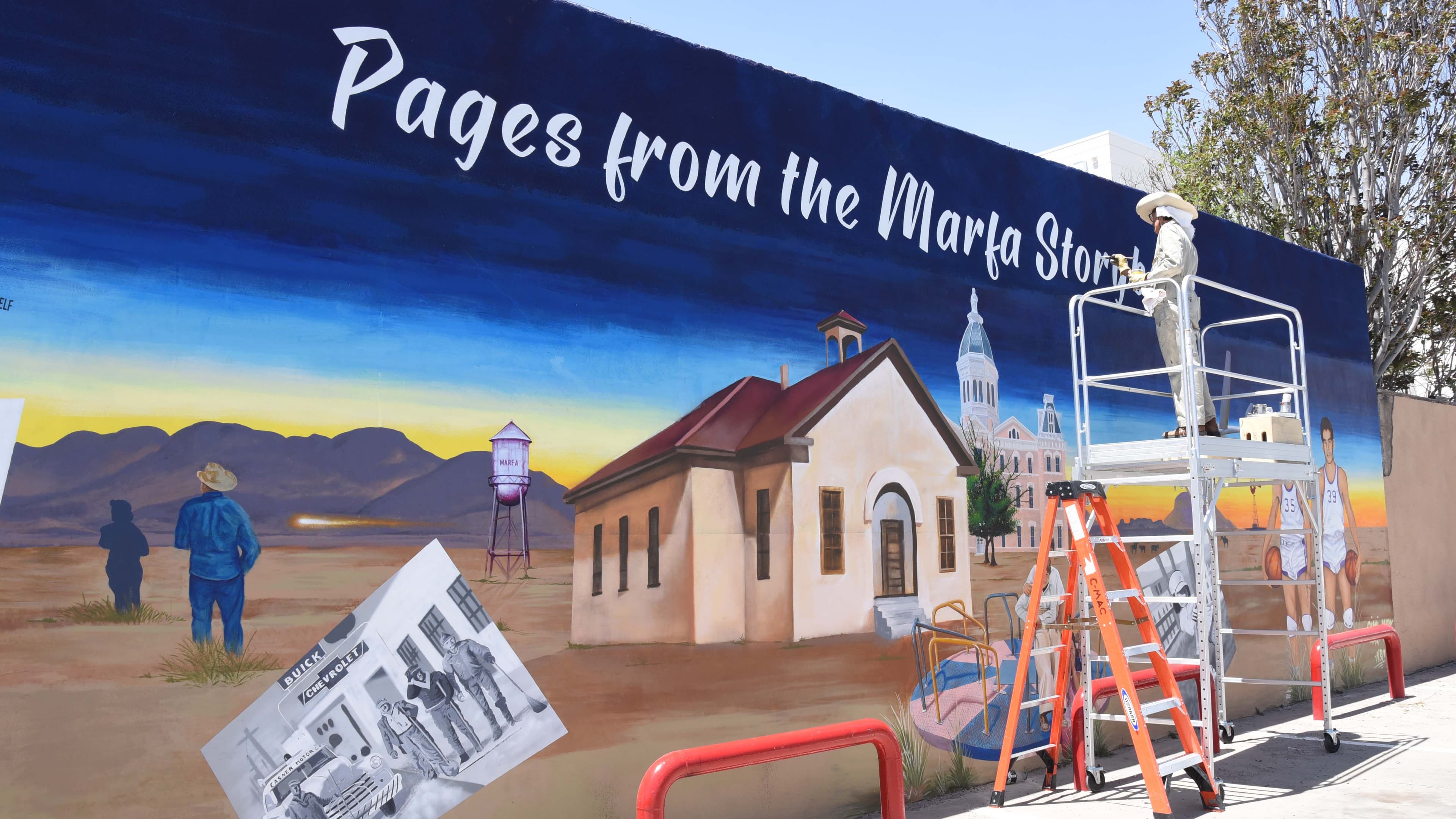 A painter works on a mural of a school building