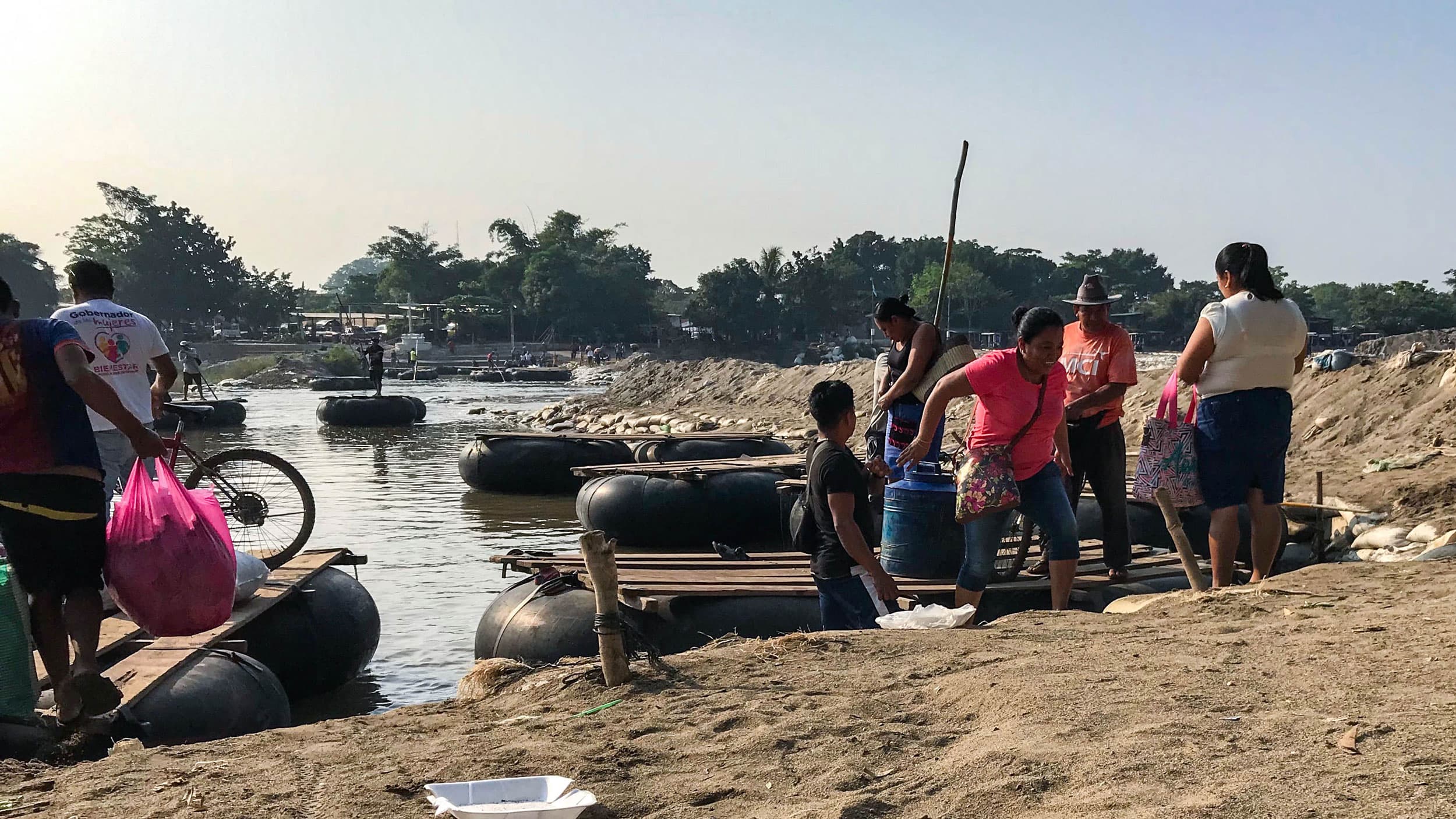 Several people are shown on the beach next to large floating rafts with wooden tops.
