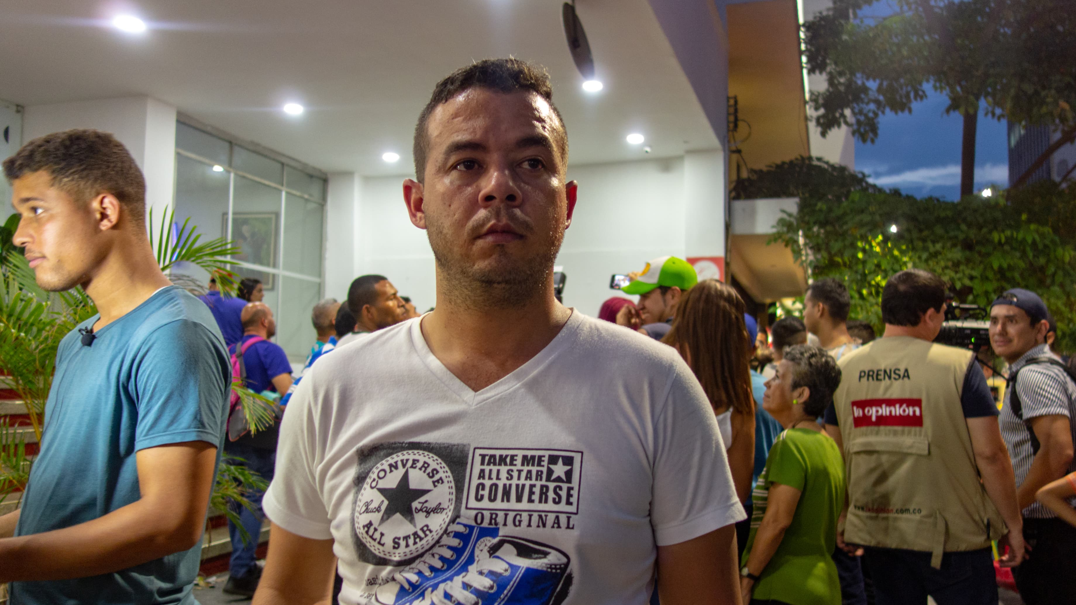 Man stands wearing white shirt in front of a hotel.