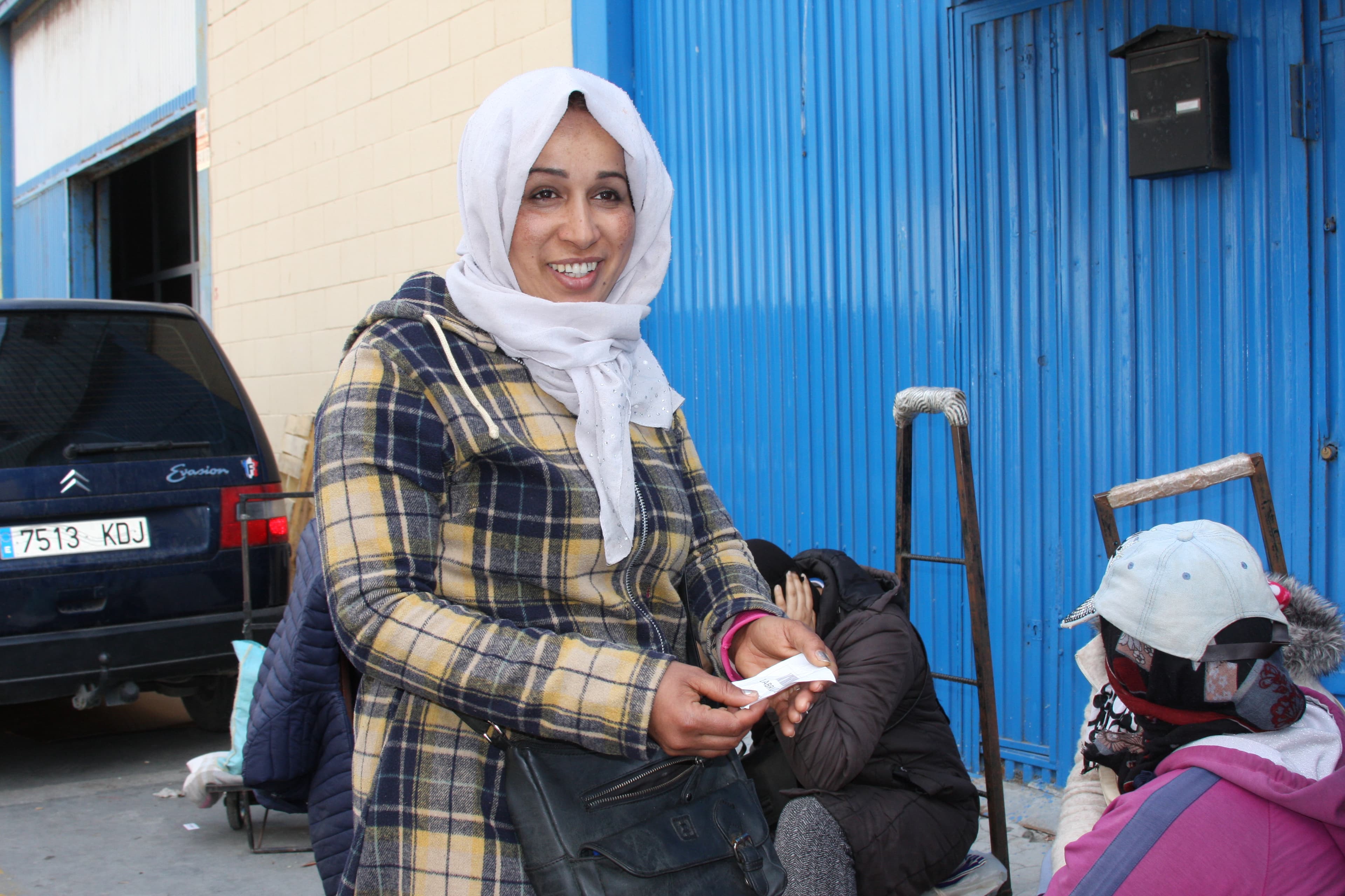 Woman in white scarf and plaid yellow jacket holds a white ticket in her hand