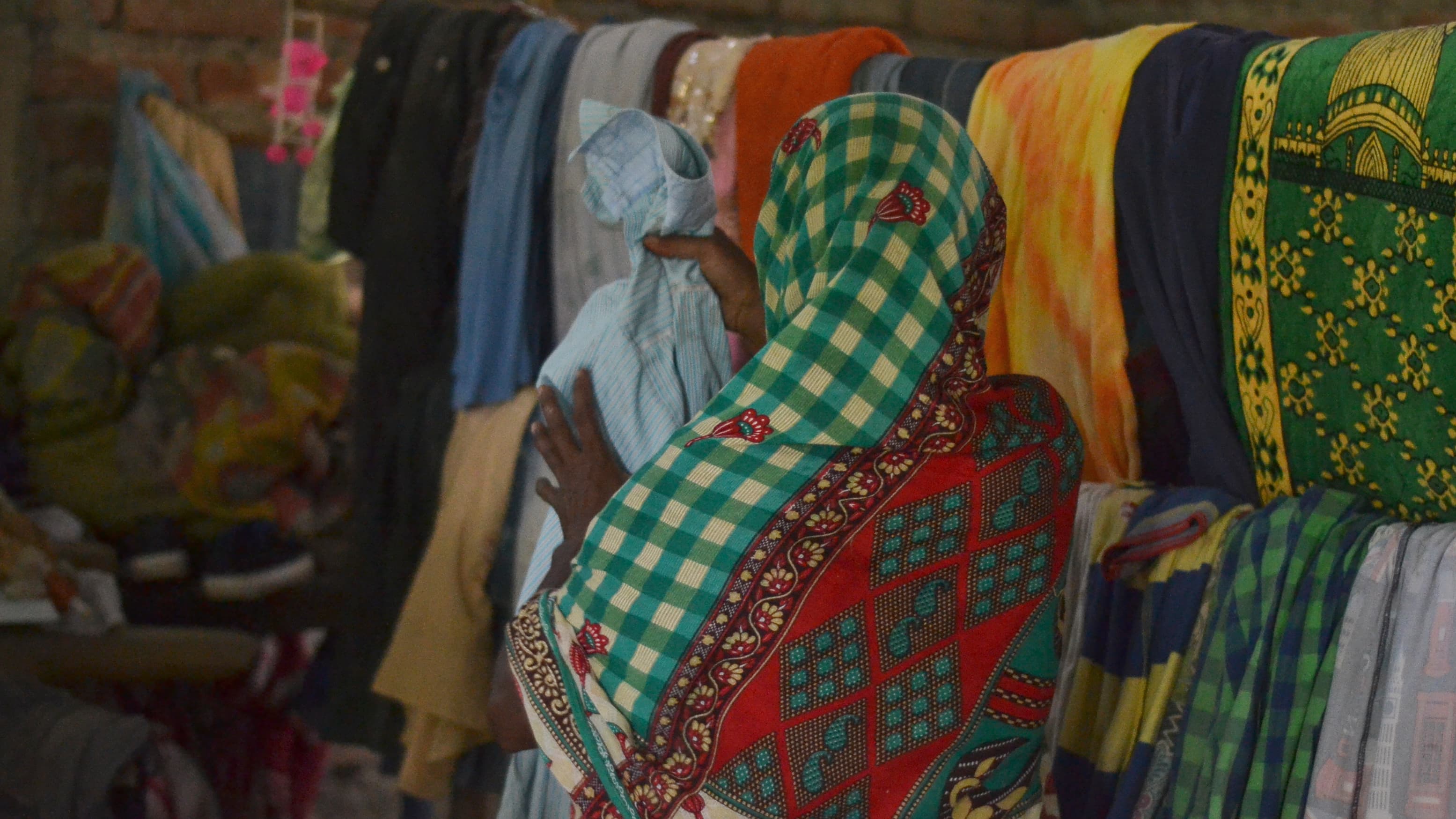 A woman stands with her back to the camera wearing a plaid green and yellow scarf.
