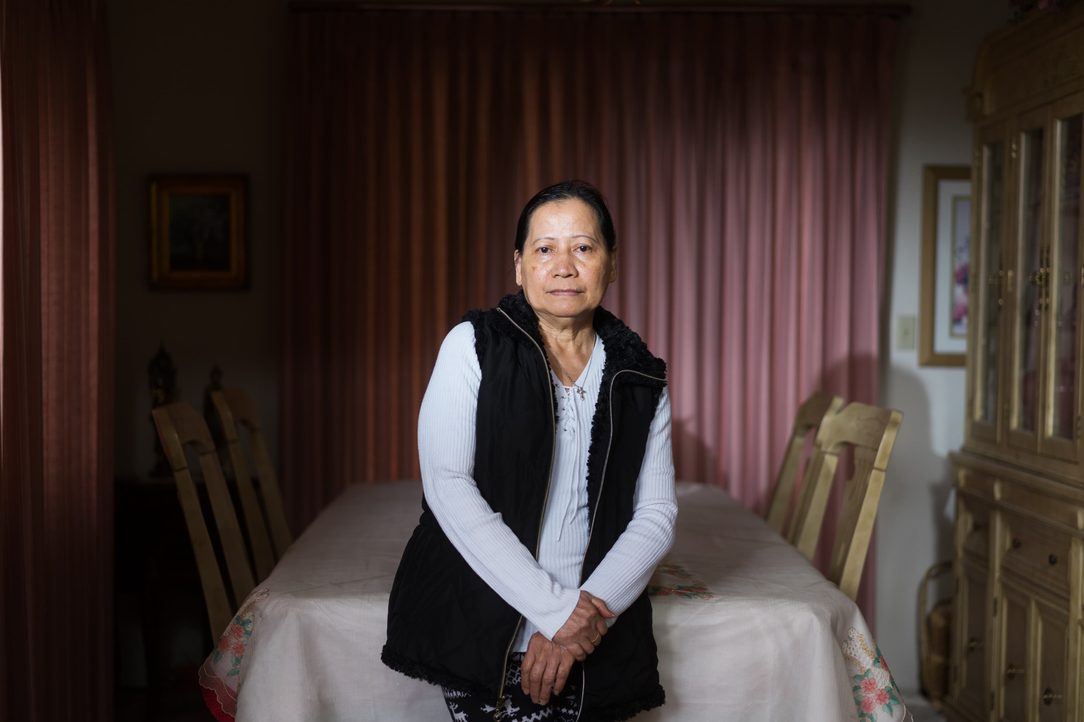 An old woman stands in front of a table in a home.