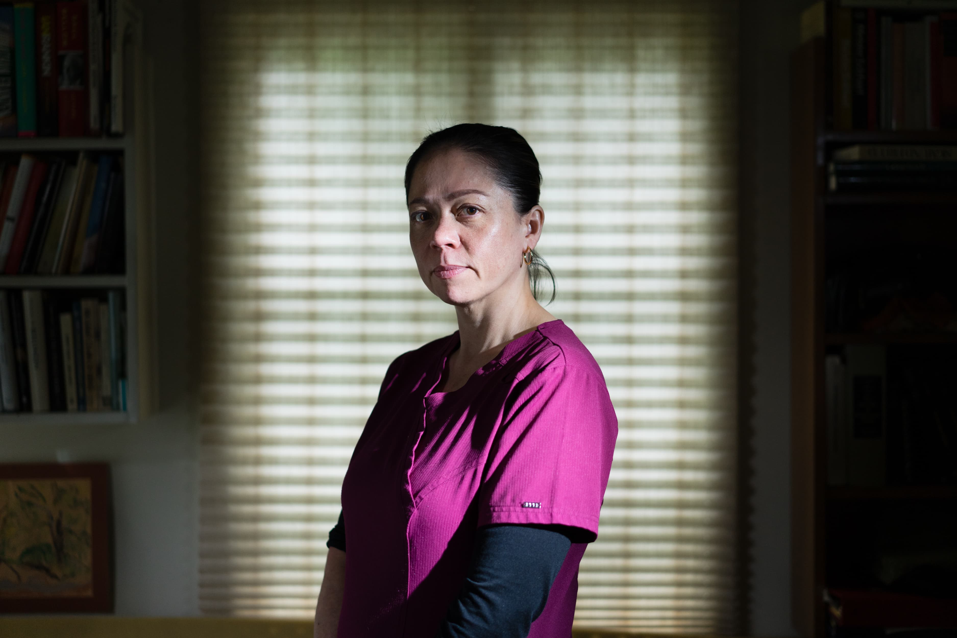 A woman stands in front of a window inside a home.