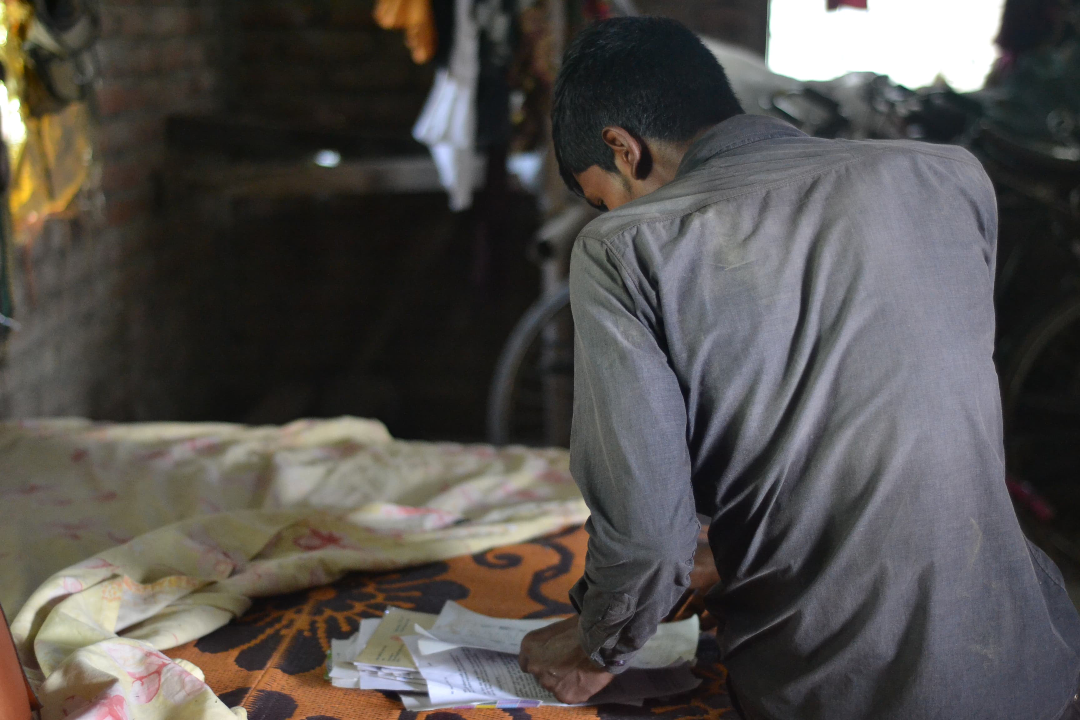 A young man sits on a bed reading over documents.